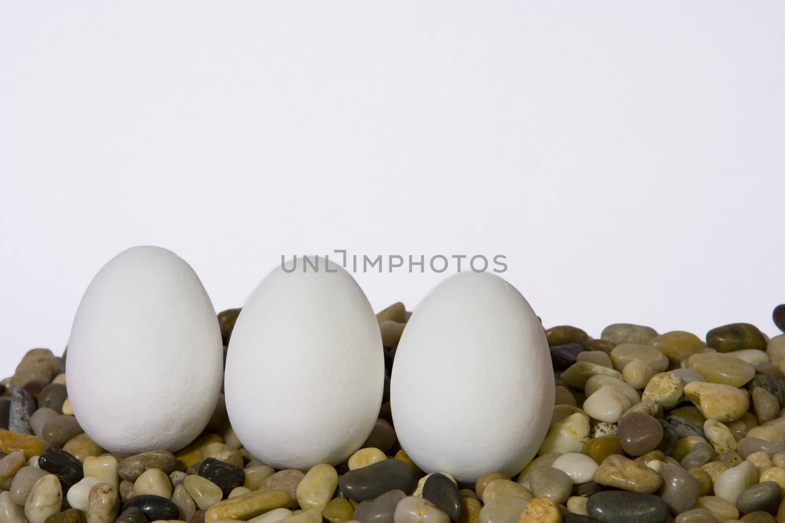 Three white easter eggs on pebbles against white background