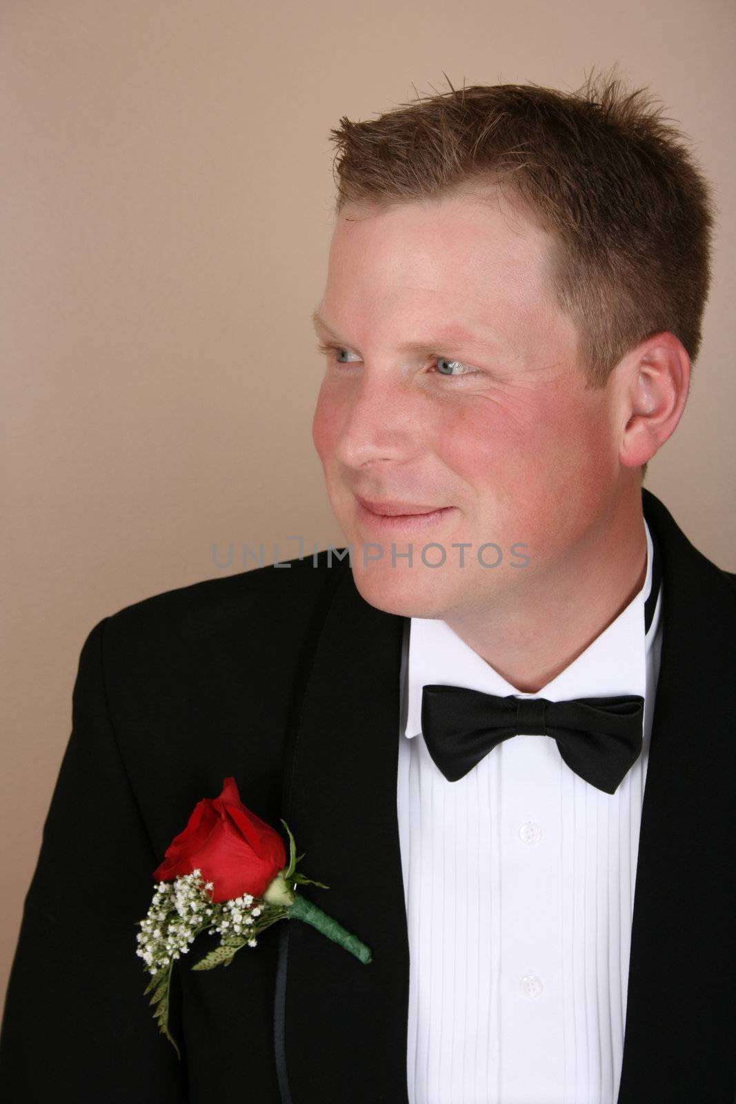 Smiling groom on his wedding day wearing a red rose corsage 