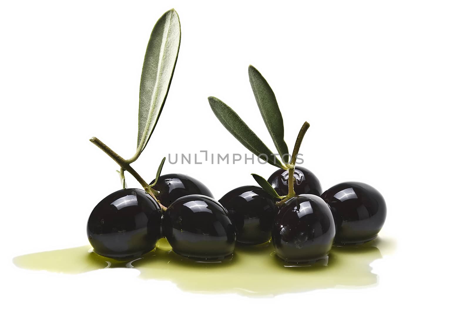 Premium black olives with leaves covered in olive oil and isolated over a white background.