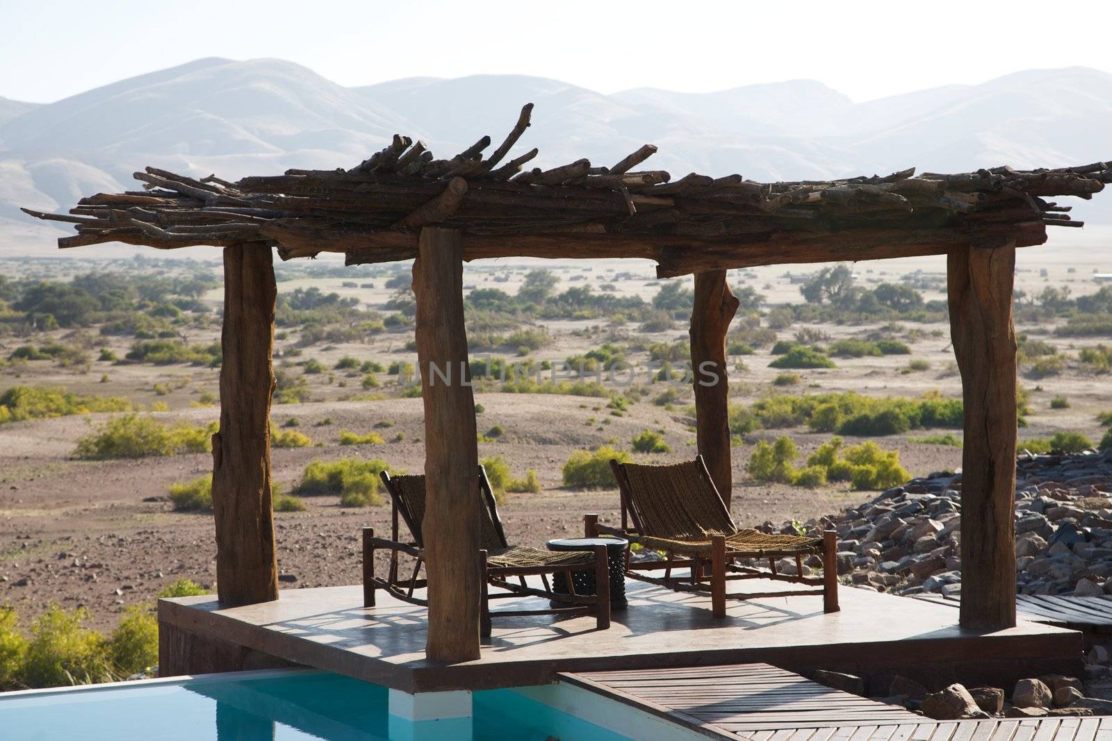 Relax chairs under a wood roof and a swimming pool facing the desert of Namibia