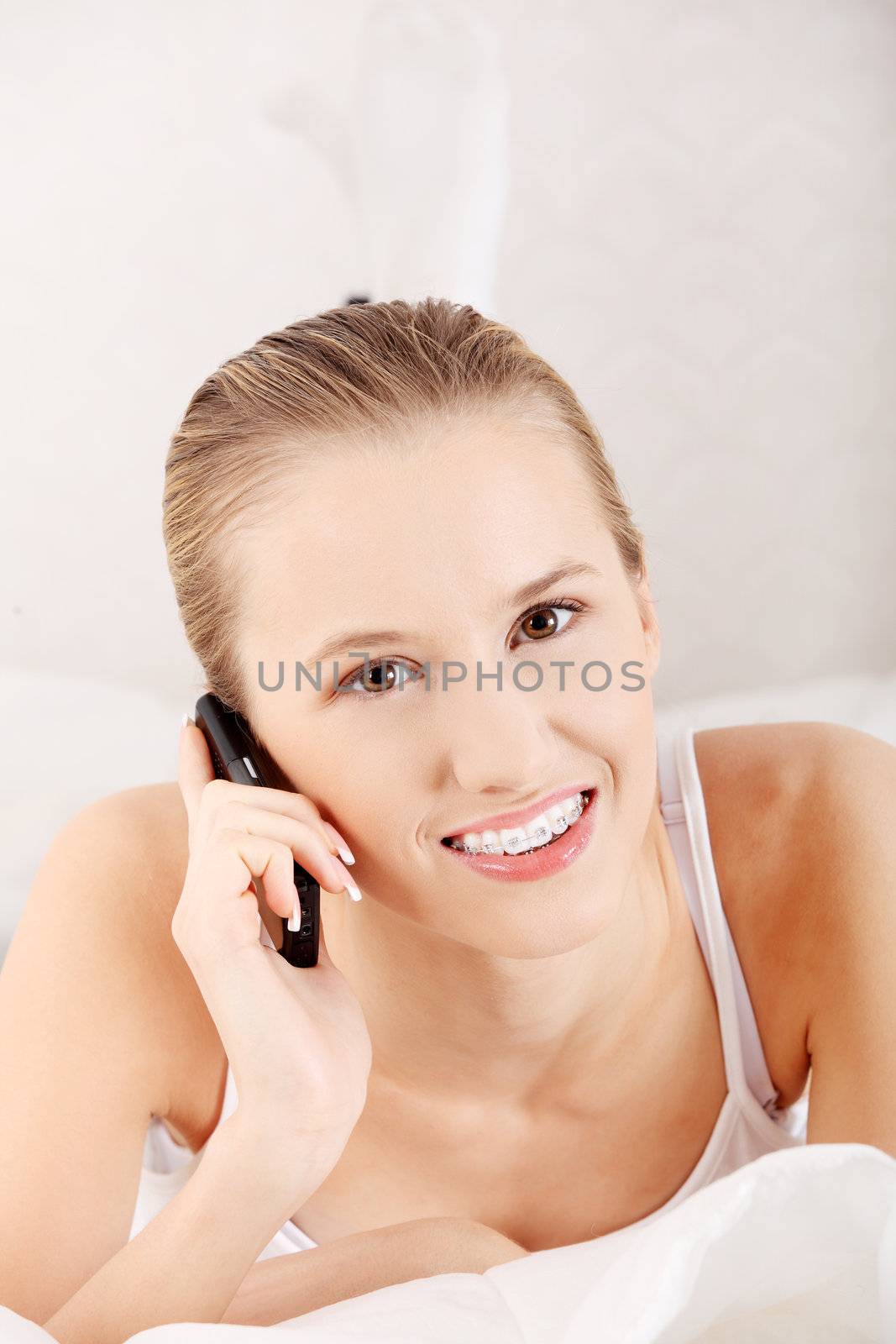 Pretty woman with mobile phone lying on bed at home