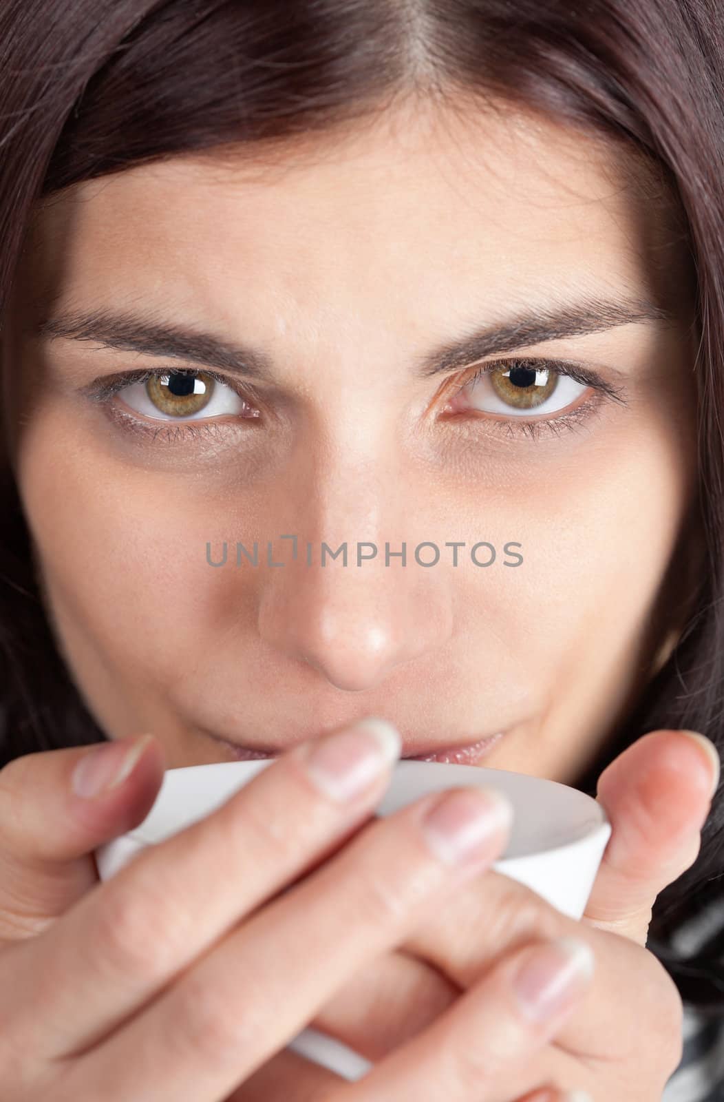 Closeup portrait of young brunette woman holding a cup of coffee close to her lips