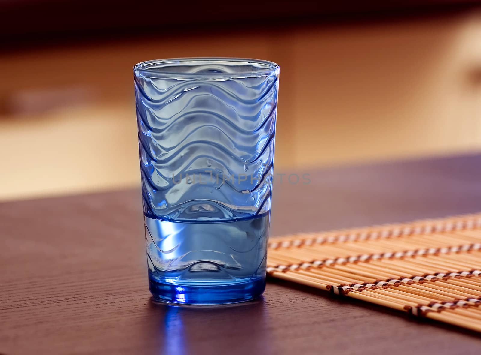 Photo of a half empty cold water glass on a modern wooden table