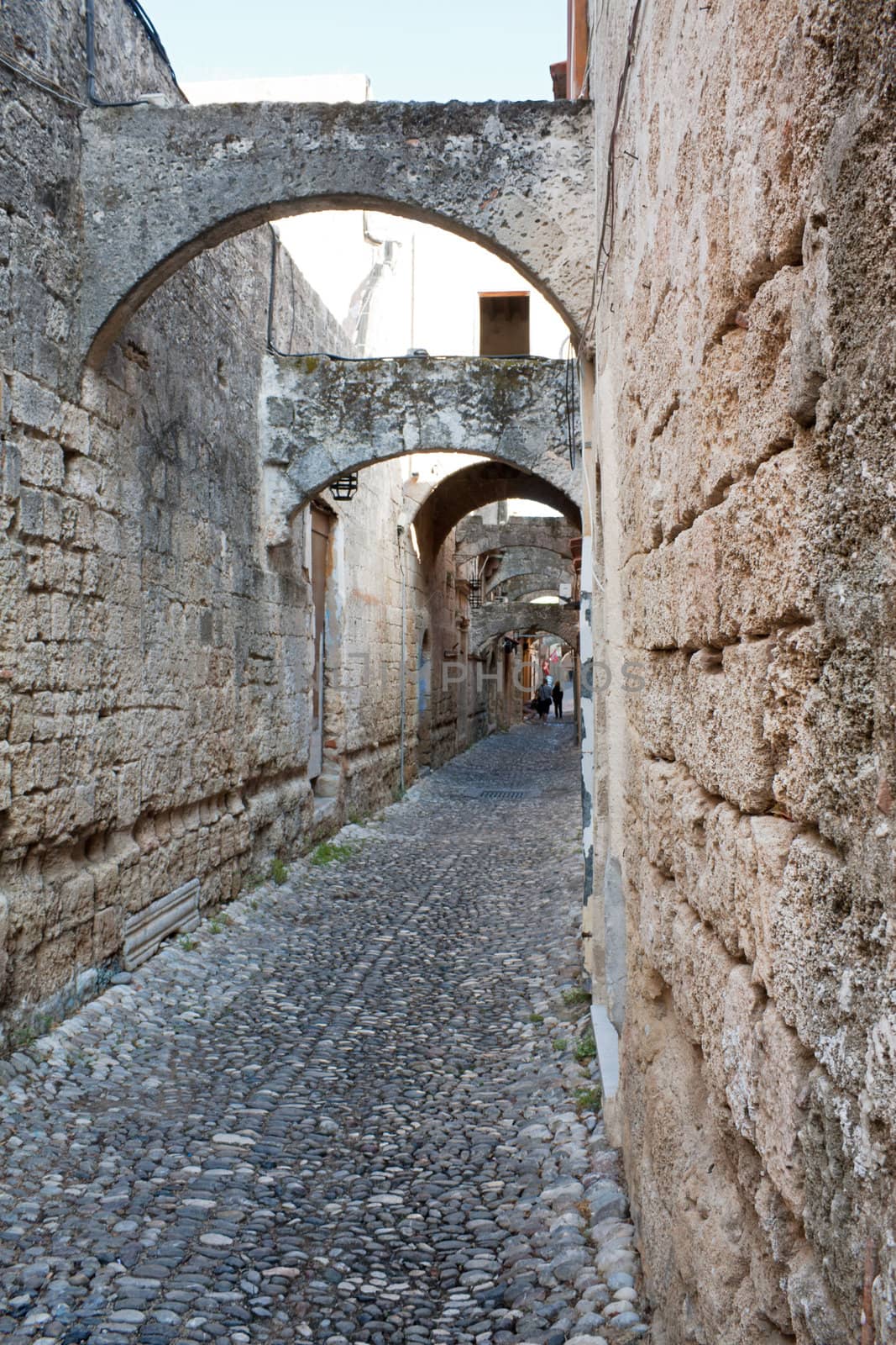 A medieval cobblestone alley in Rhodes Old Town (UNESCO World Heritage Site), Greece, with arches and stone facades.