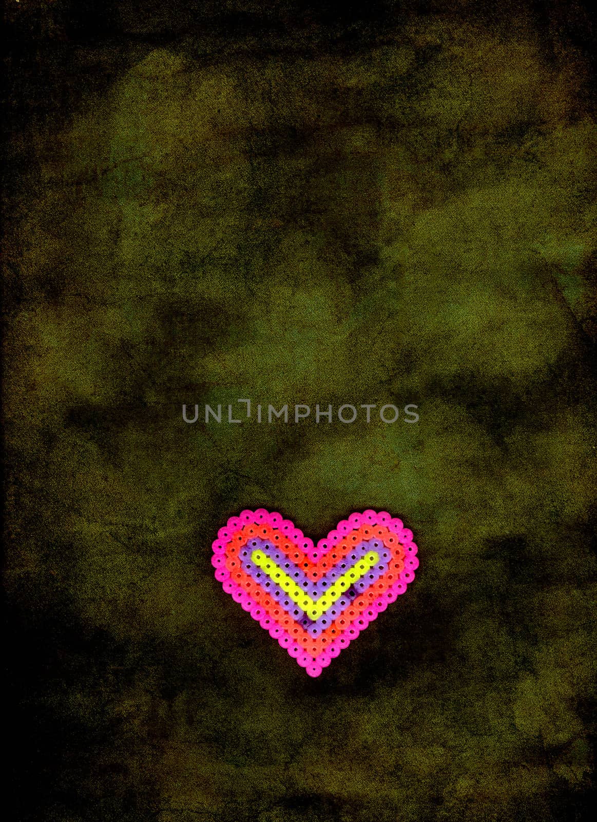 A pink heart made by a child floating on green background.