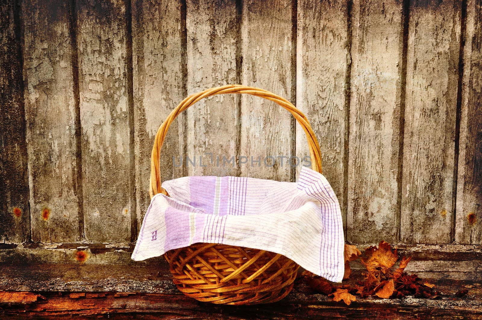 Picnic basket with autumn leaves aganst an old wooden wall.