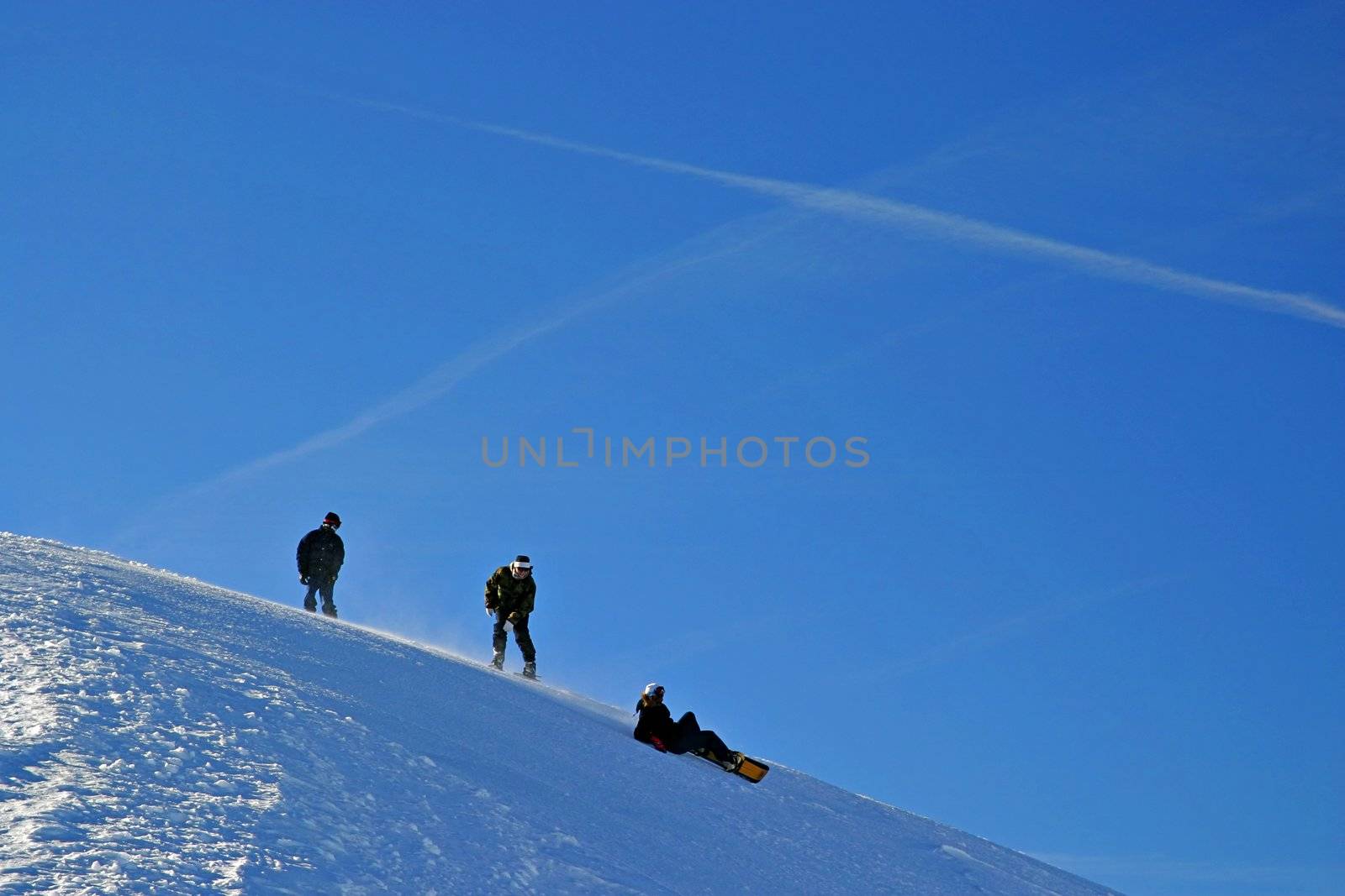 Snowboarders on slope, with blue sky.