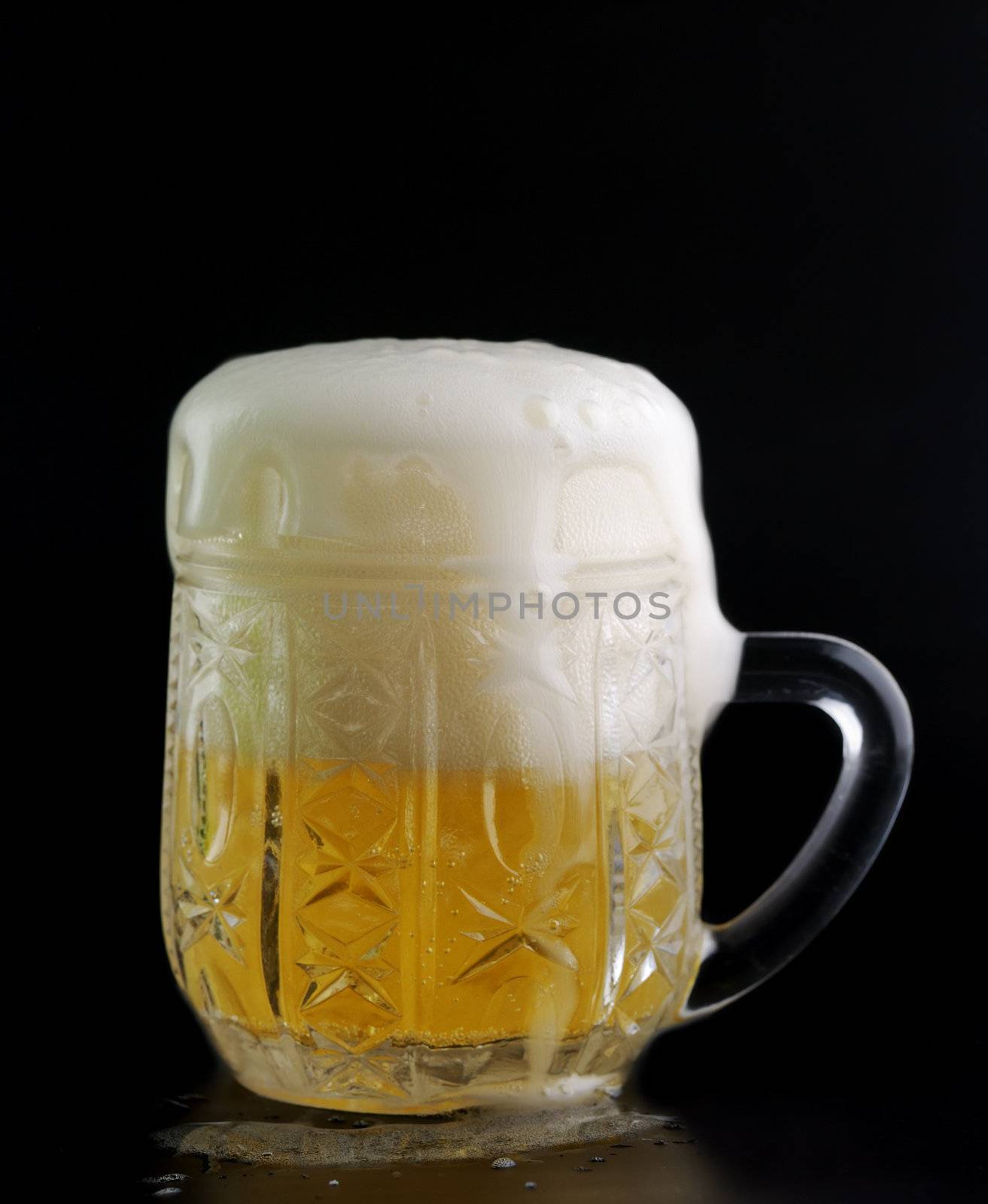 Glass of beer on a black background with the foam poured around