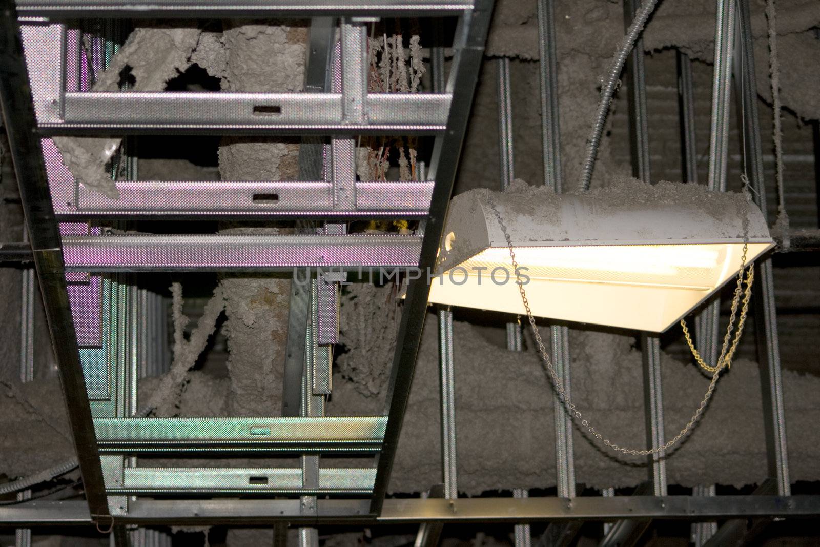 Industrial Rafters Construction Dust is a capture of an exposed area. There is a mix of insulation and dust visible next to a light that is creating a rainbow effect on the structure that looks like a ladder.
