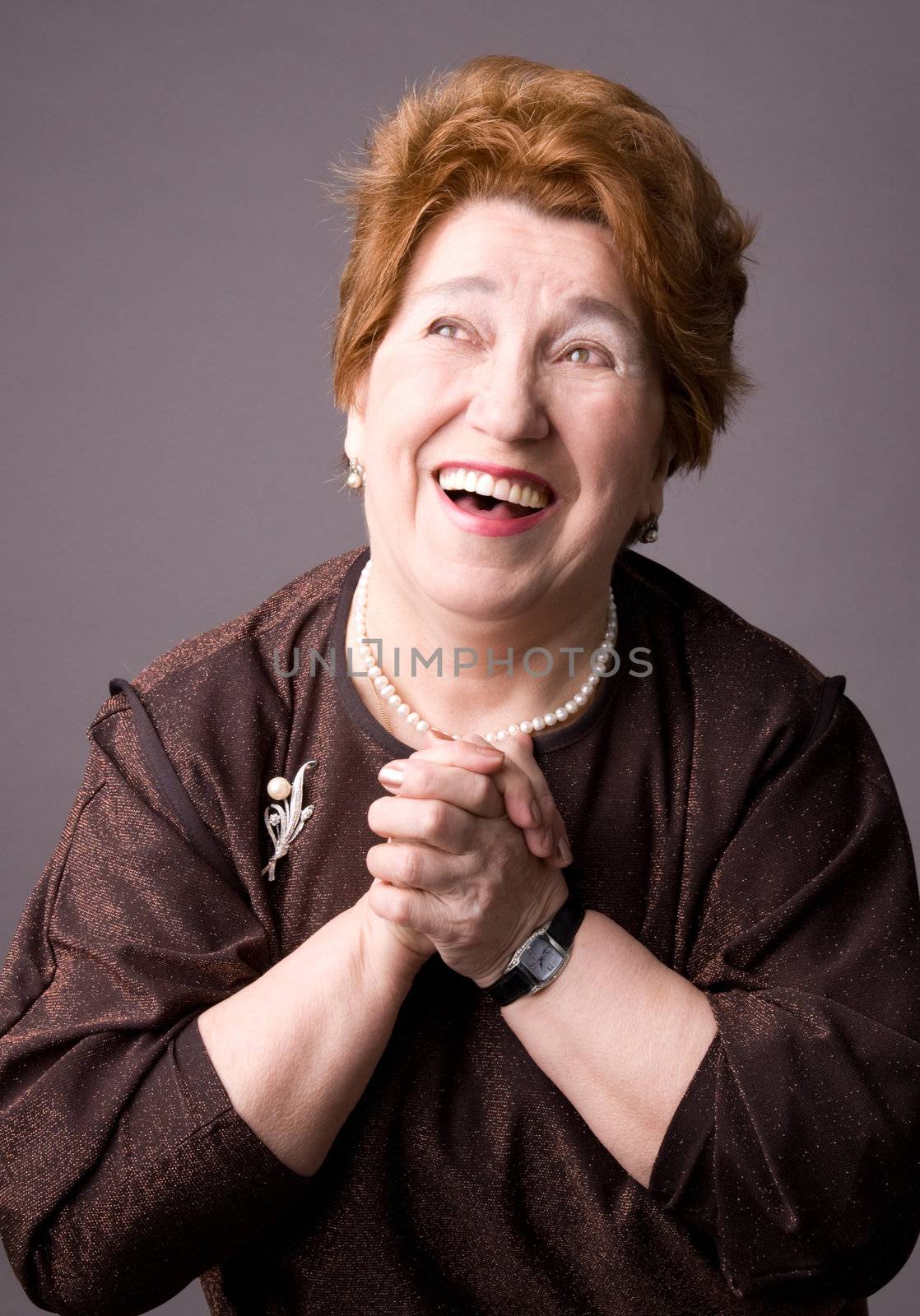 The cheerful elderly woman in a brown dress on a grey background.