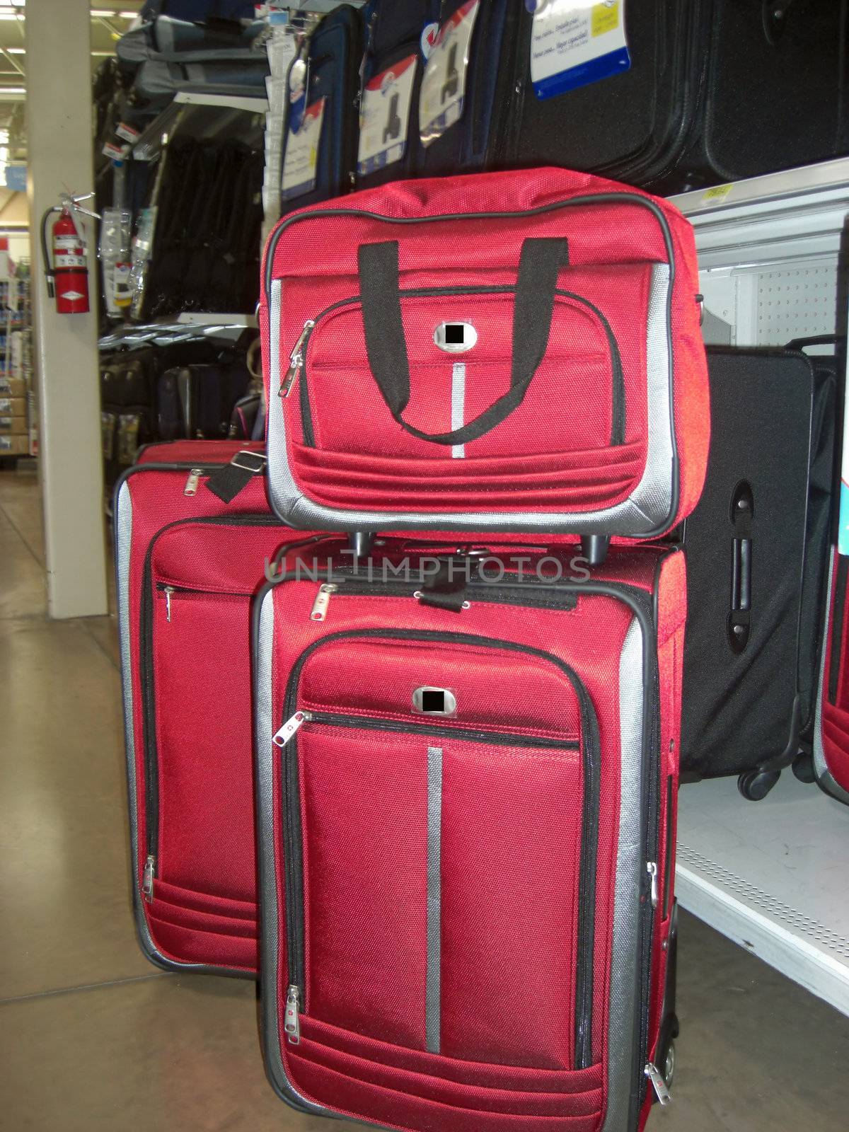 A set of red travelling bags are displayed in front of black and navy blues bags in a luggage store