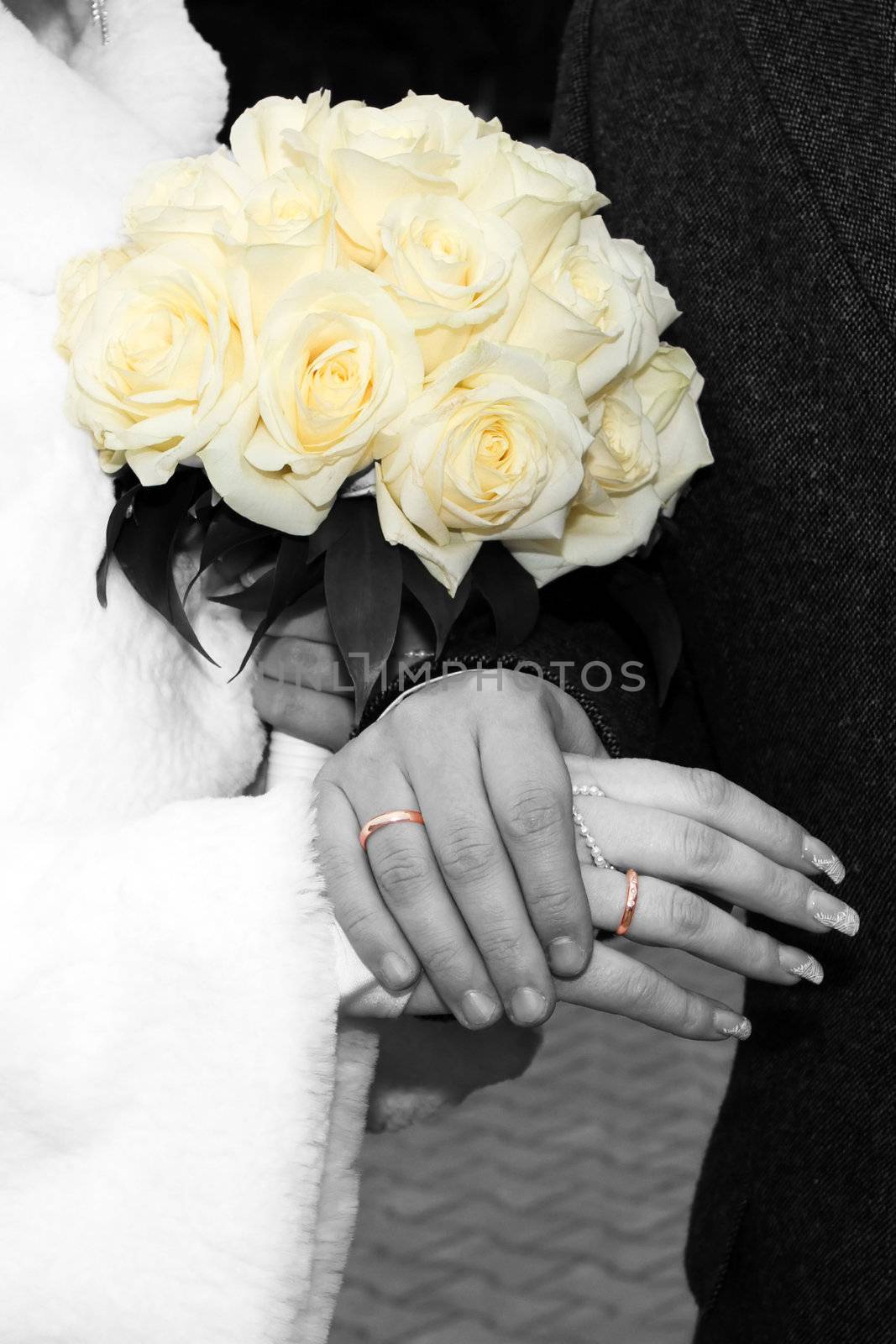 Wedding bouquet and groom's and bride's hands with wedding rings. Black and white photo with color accent