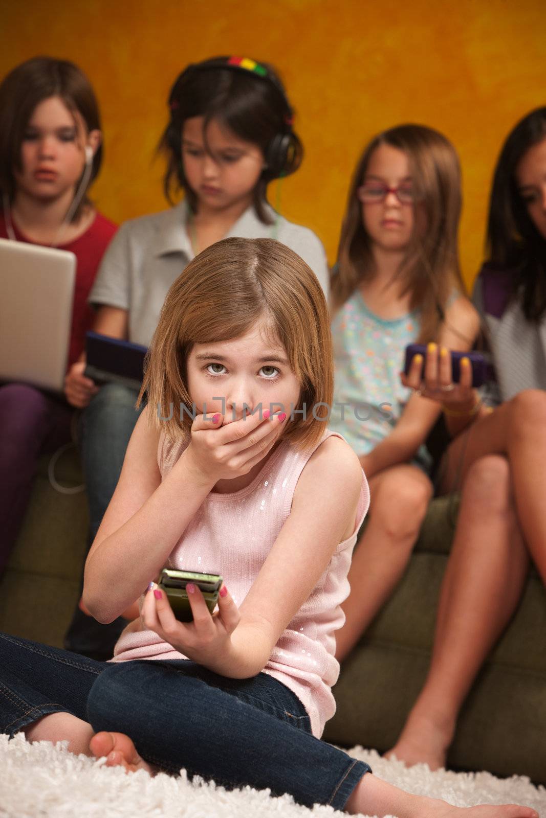 Little Caucasian girl with handheld device covers her mouth