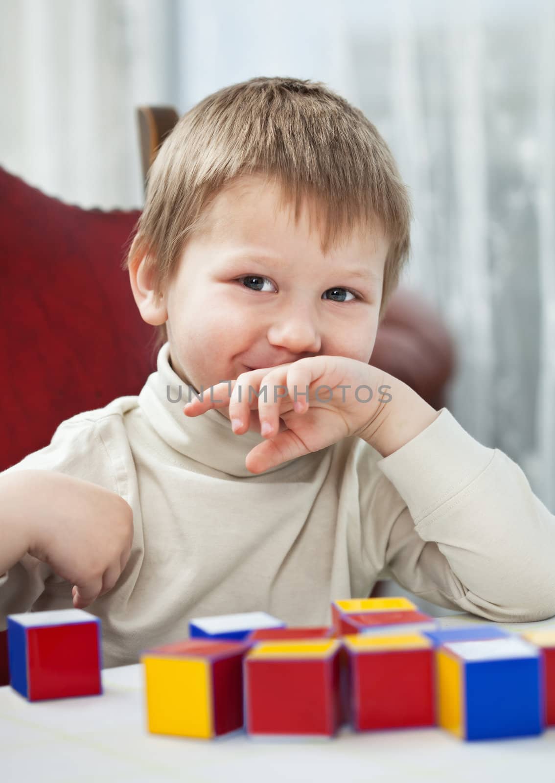 Smiling blond boy seating at the table with colorful blocks