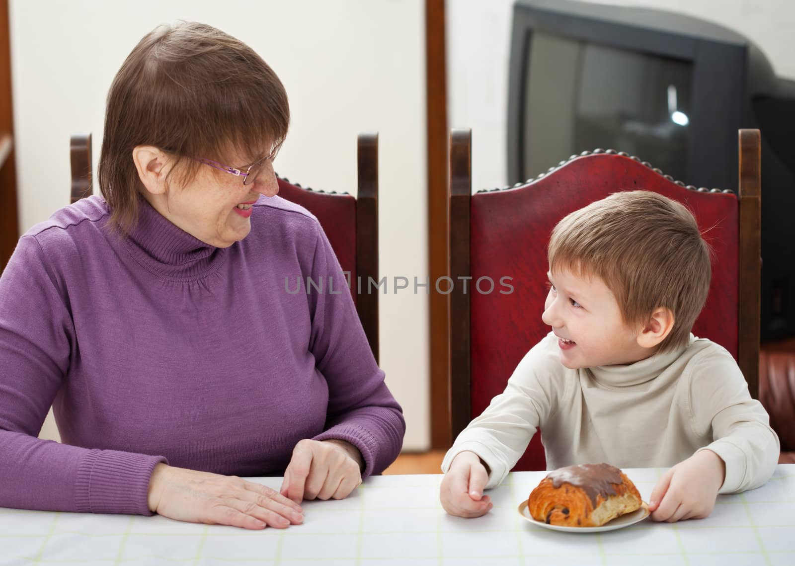 Smiling grandson and his granny sitting at the table at home