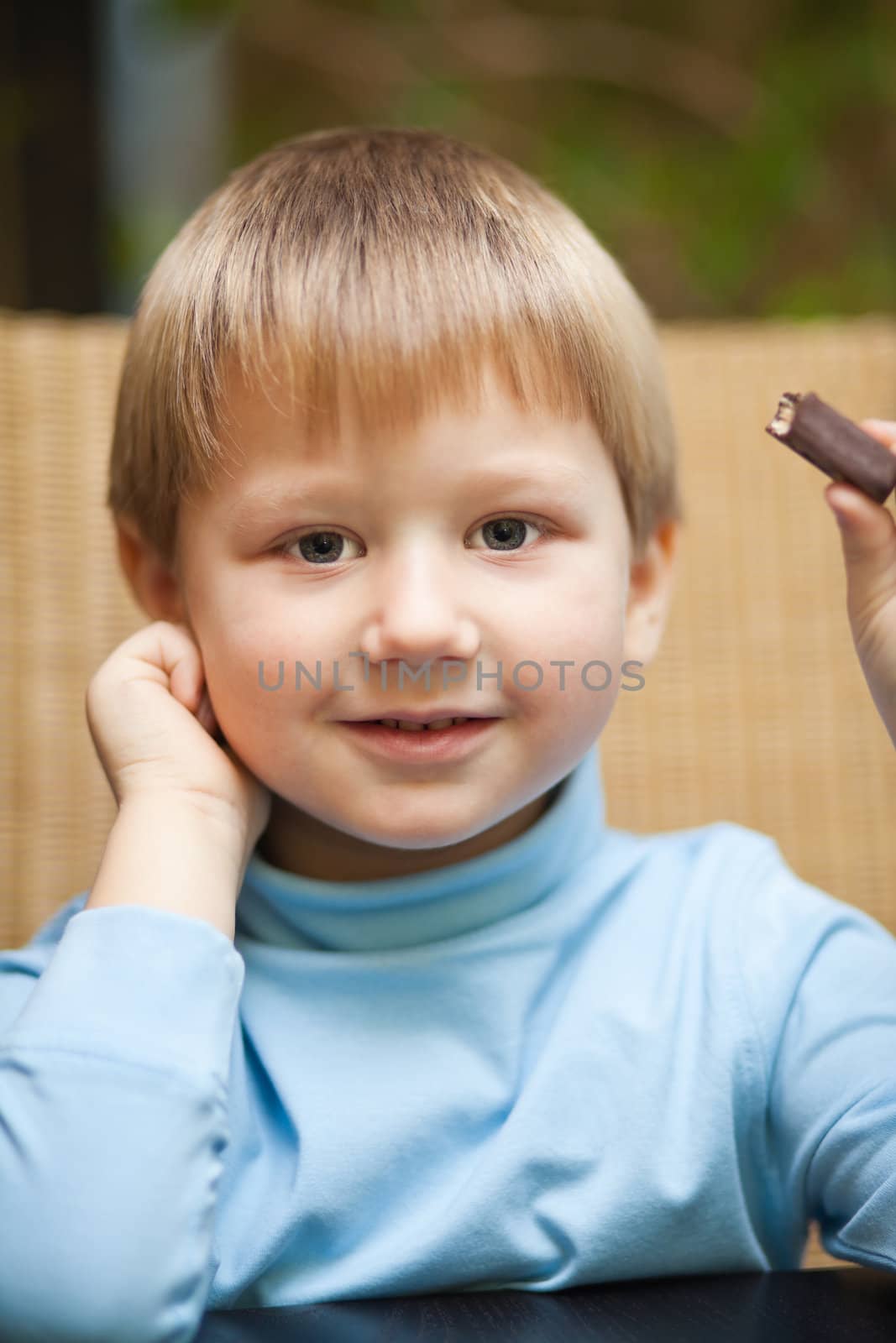Cute smiling blond boy holding a chocolate candy