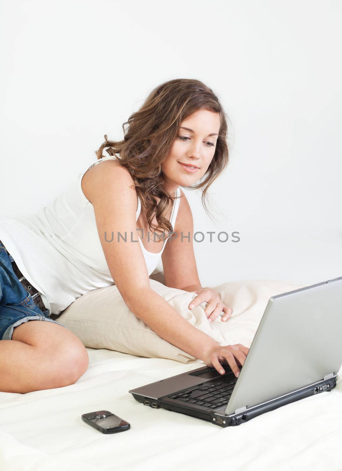 Pretty young woman her bed with laptop computer and cellphone