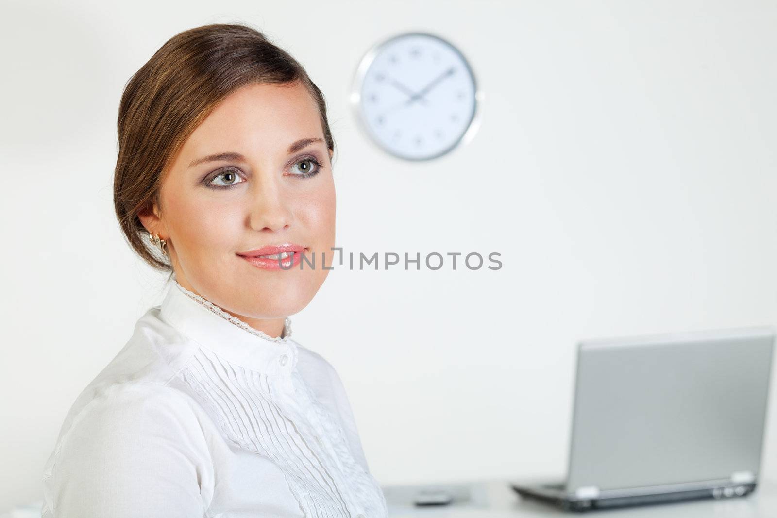 Young pretty smiling businesswoman standing in front of her desk in the office