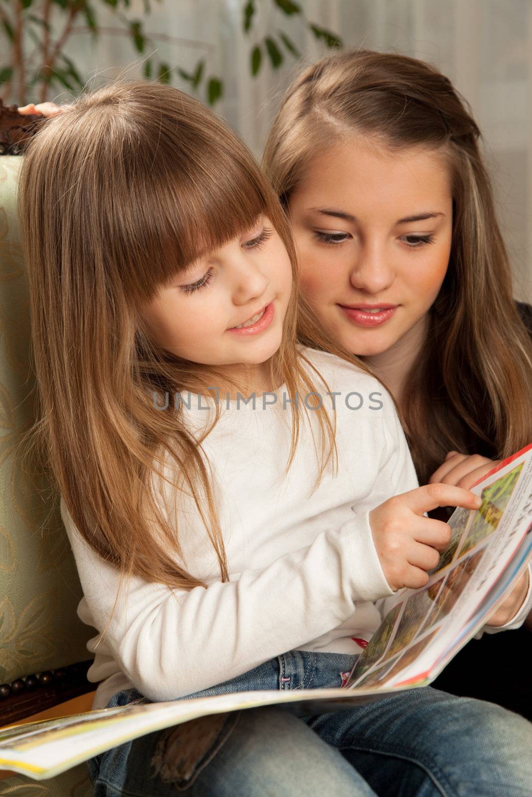 Two young sisters reading a book at home