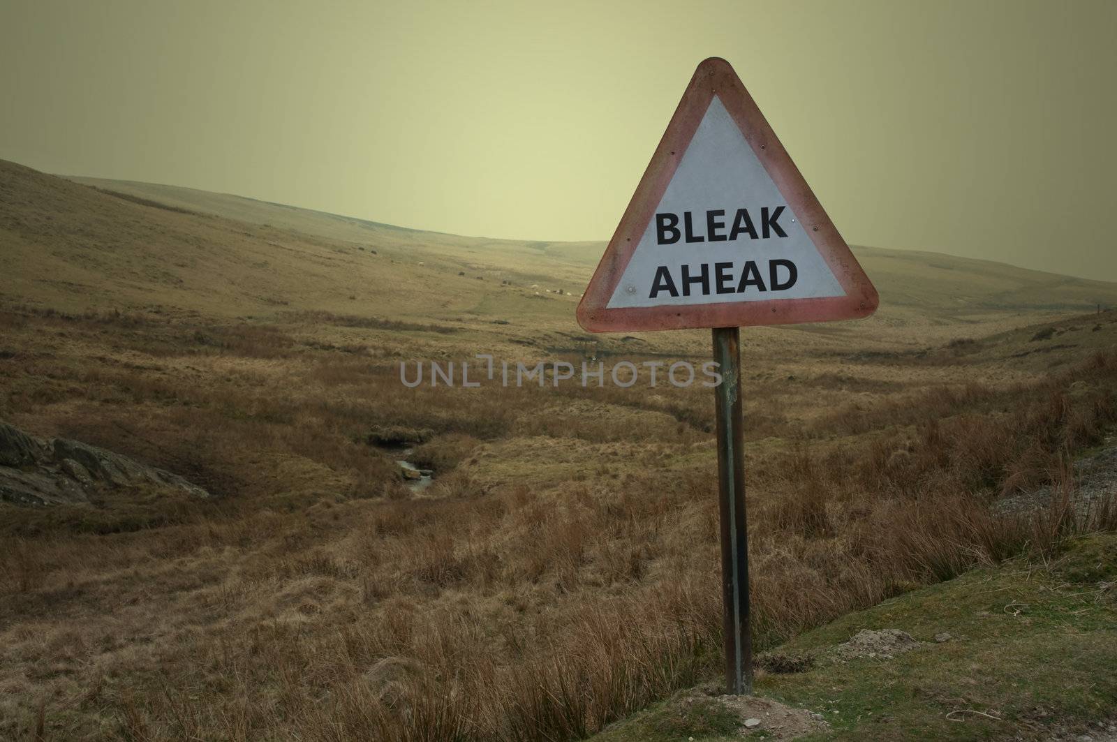 A single weathered British warning road sign with the words 'bleak ahead' against a barren moorland landscape