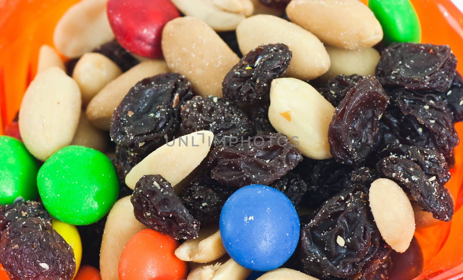 Orange cup with a closeup of trail mix on a white background.