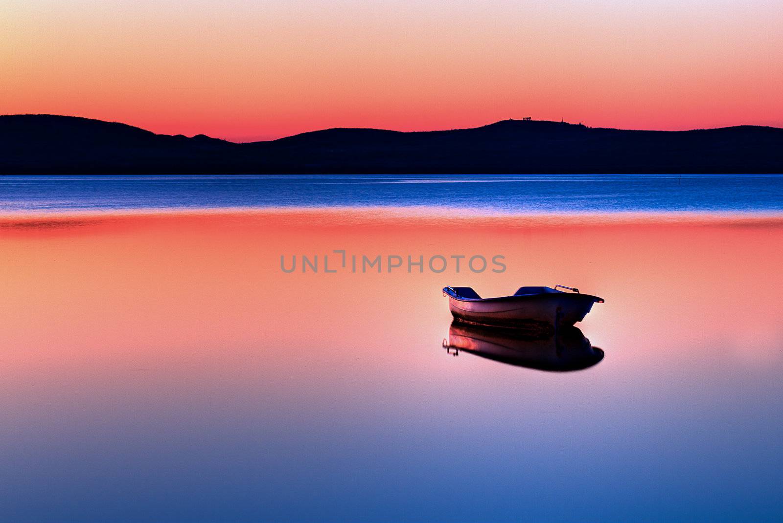 Scenic view of small fishing boat in calm water at sunset with hills in the background.