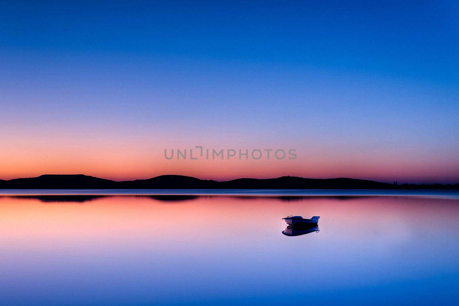 Scenic view of small fishing boat in calm water at sunset with hills in the background.