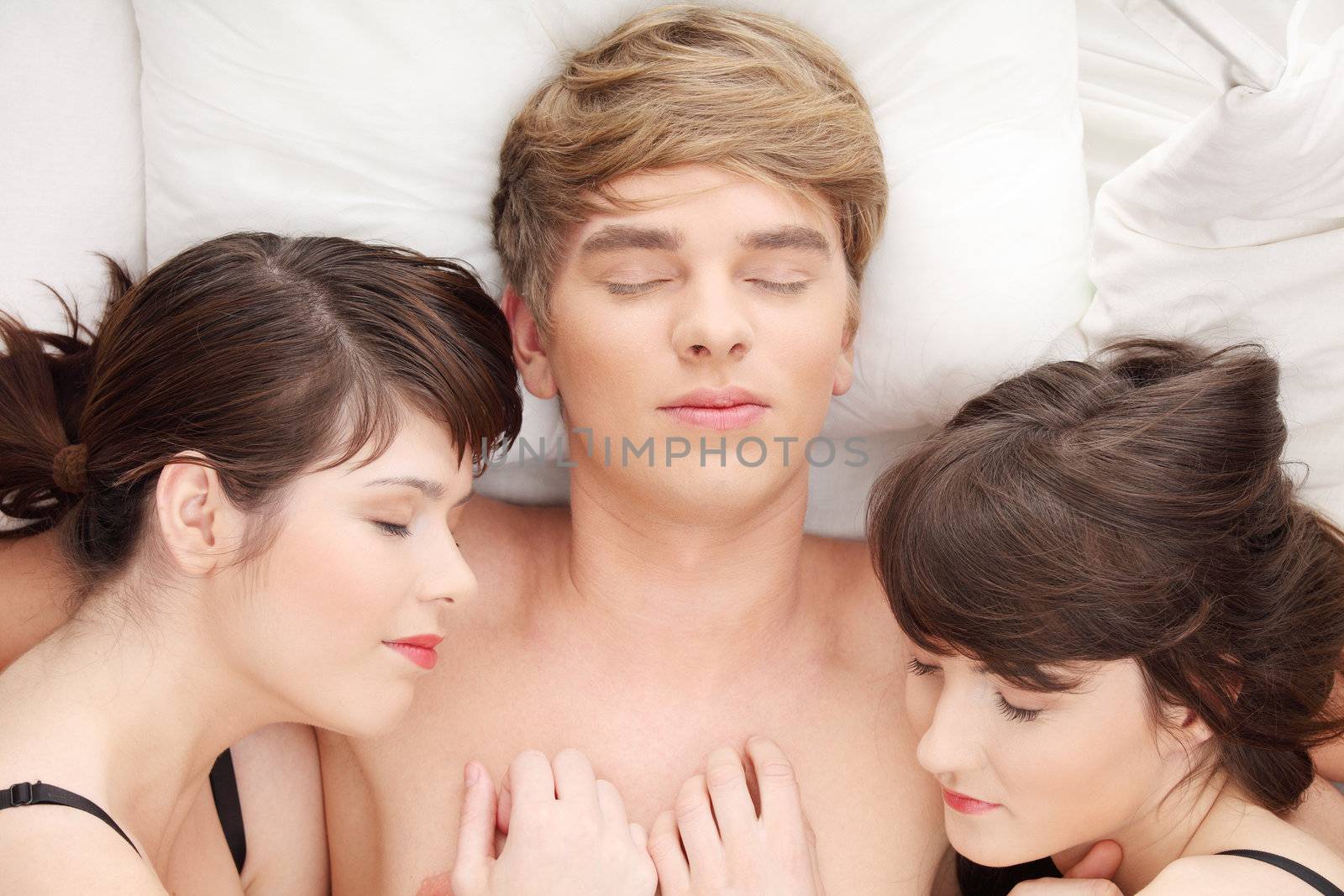 Young handsome man lying in bed with two girls