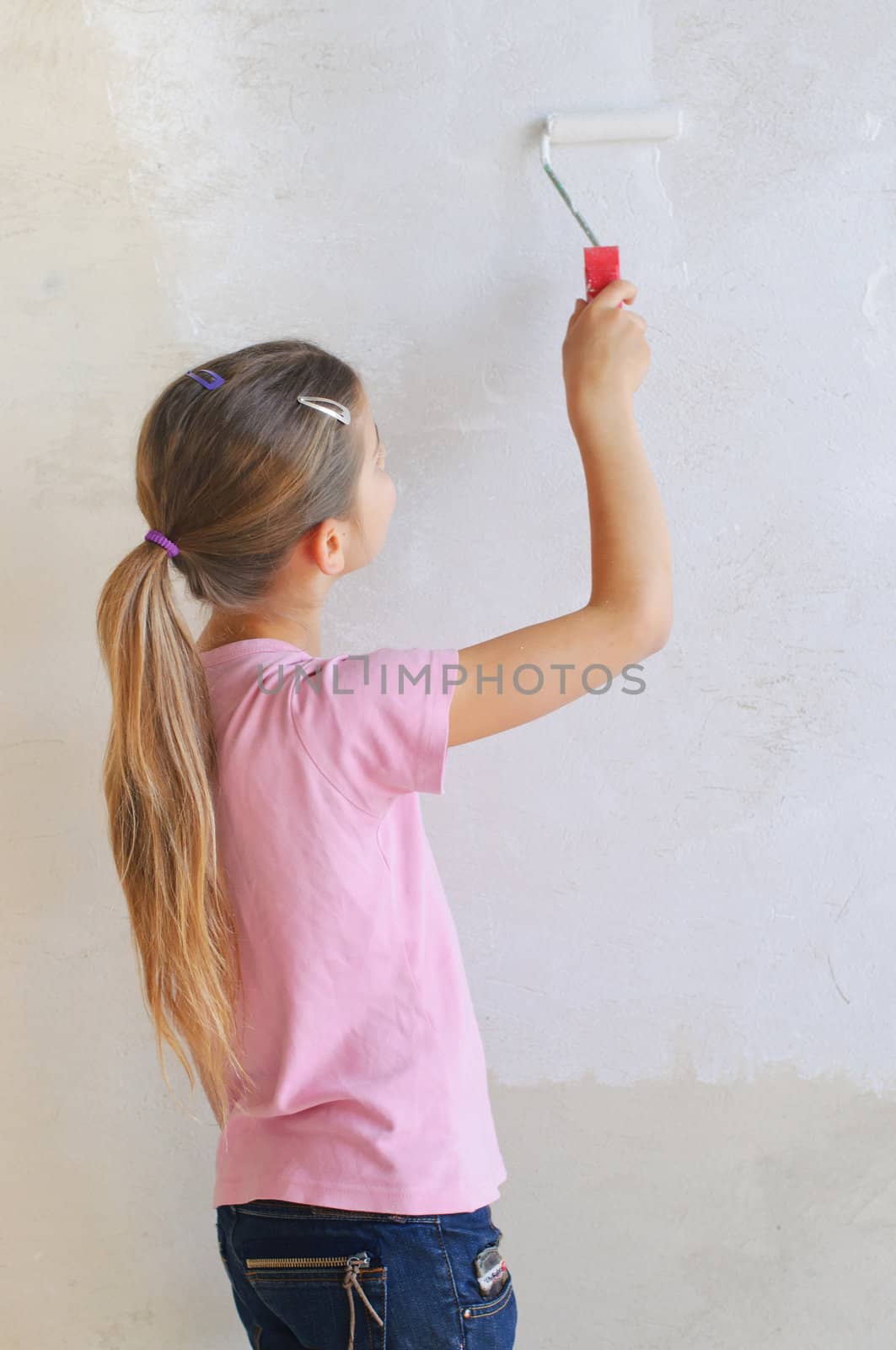 Girl painting a wall with roller .