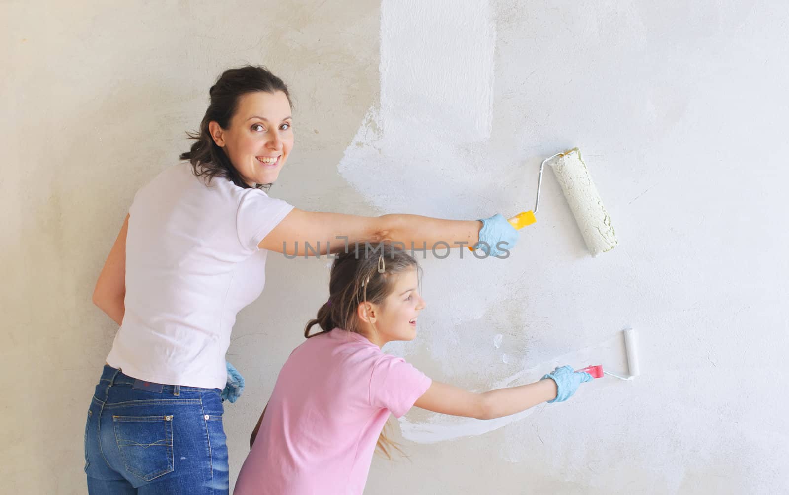 Happy Mother and douther painting a wall with roller by maxoliki