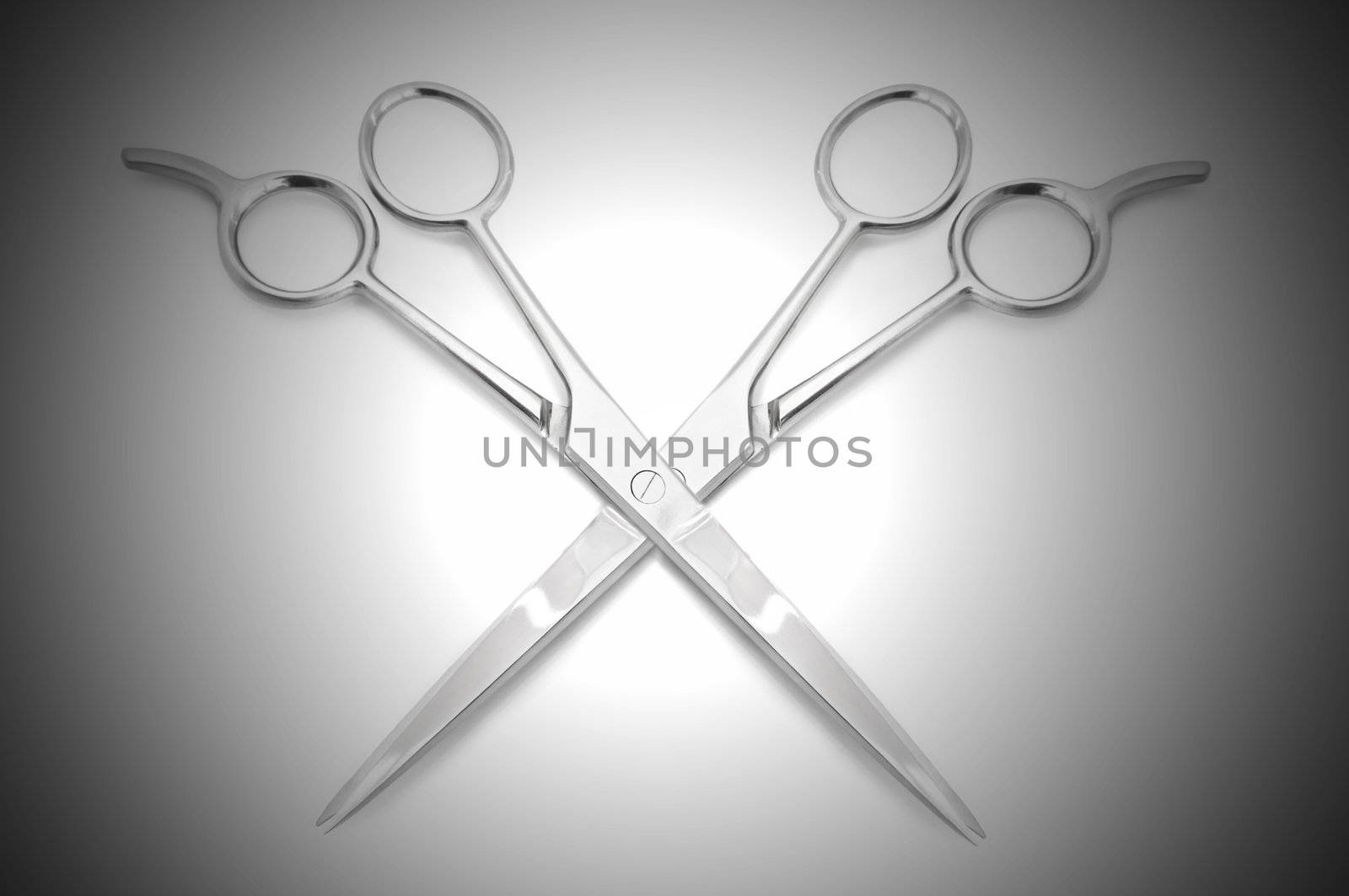 Two stainless steel hairdressing scissors overlapping each other against a white and grey light effect background