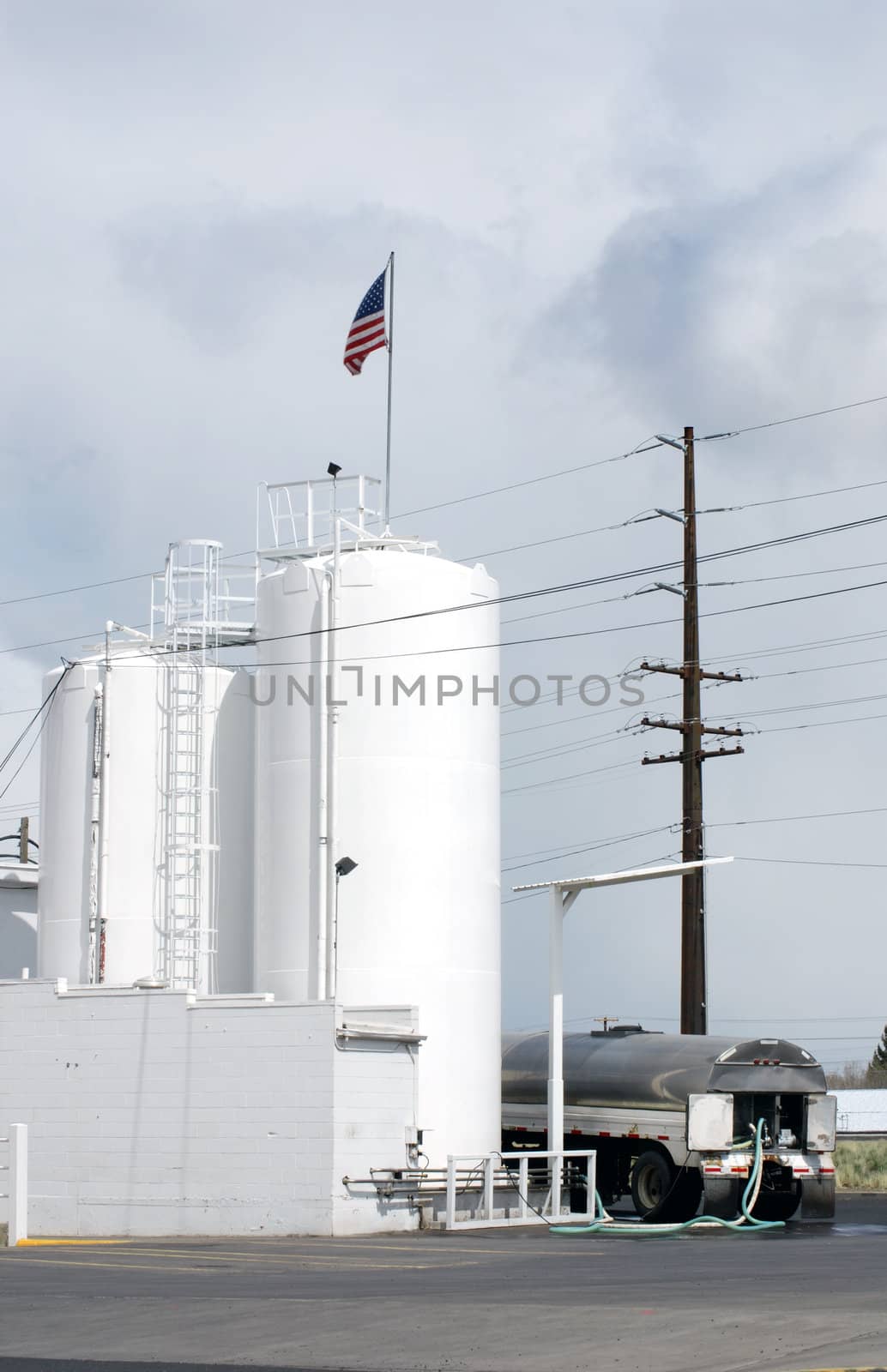 Vertical image of a tanker filling his truck from tall white silos with an American flag flying from the top.