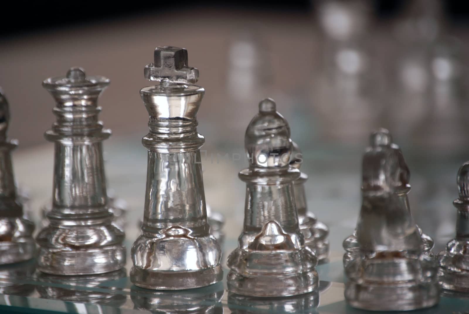 Horizontal image of a glass chess set, with focus on closest pieces and the opposing side falling out of focus in the shallow depth of field.