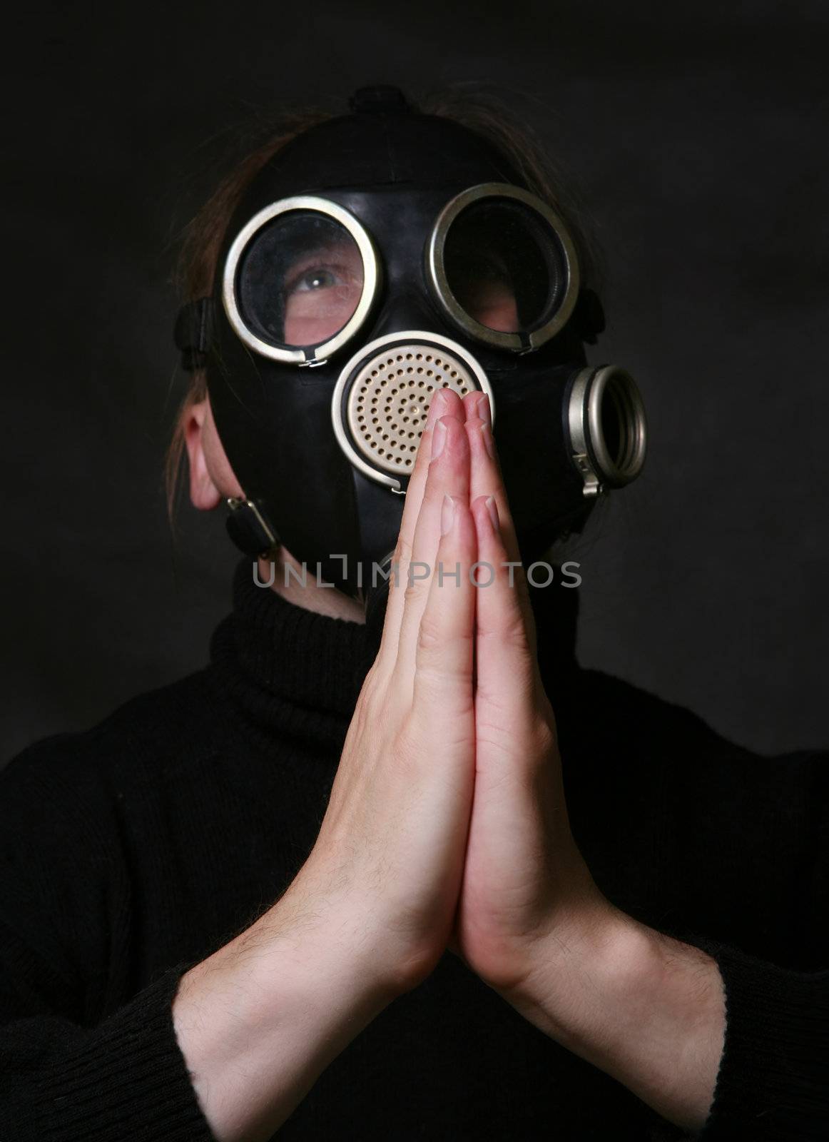 The man in a gas mask on a dark background. Hands are combined as at prayer