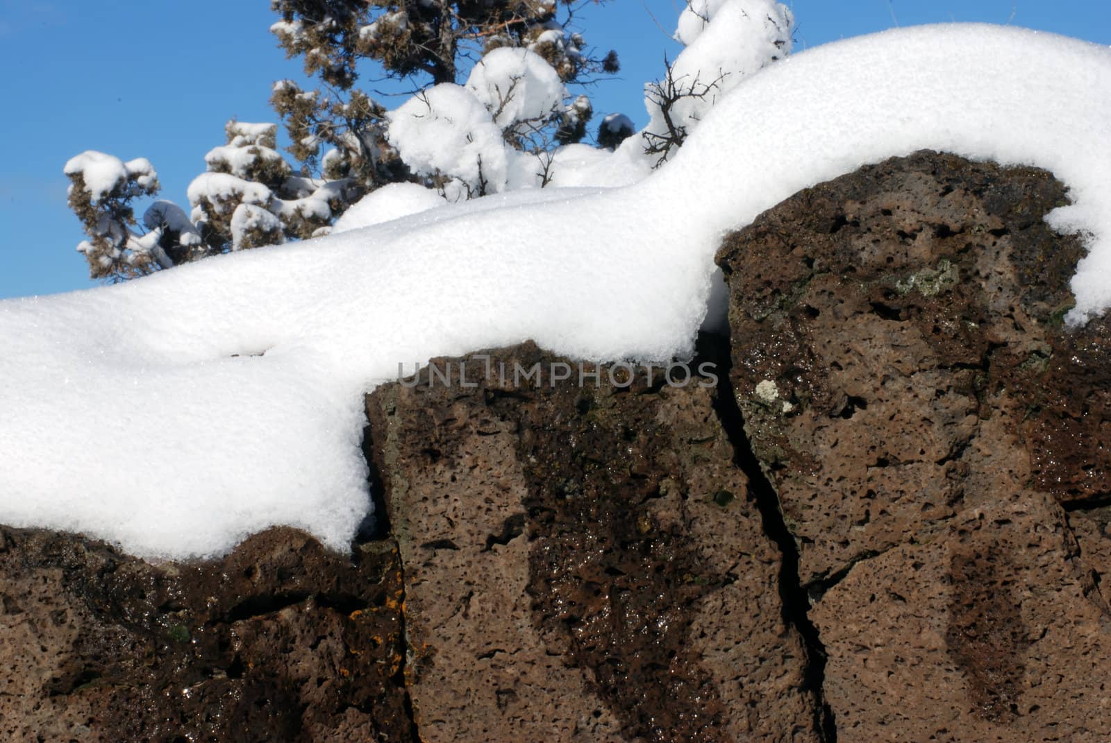 Horizontal image of fresh snow blanketing volcanic rimrock against a blue sky.