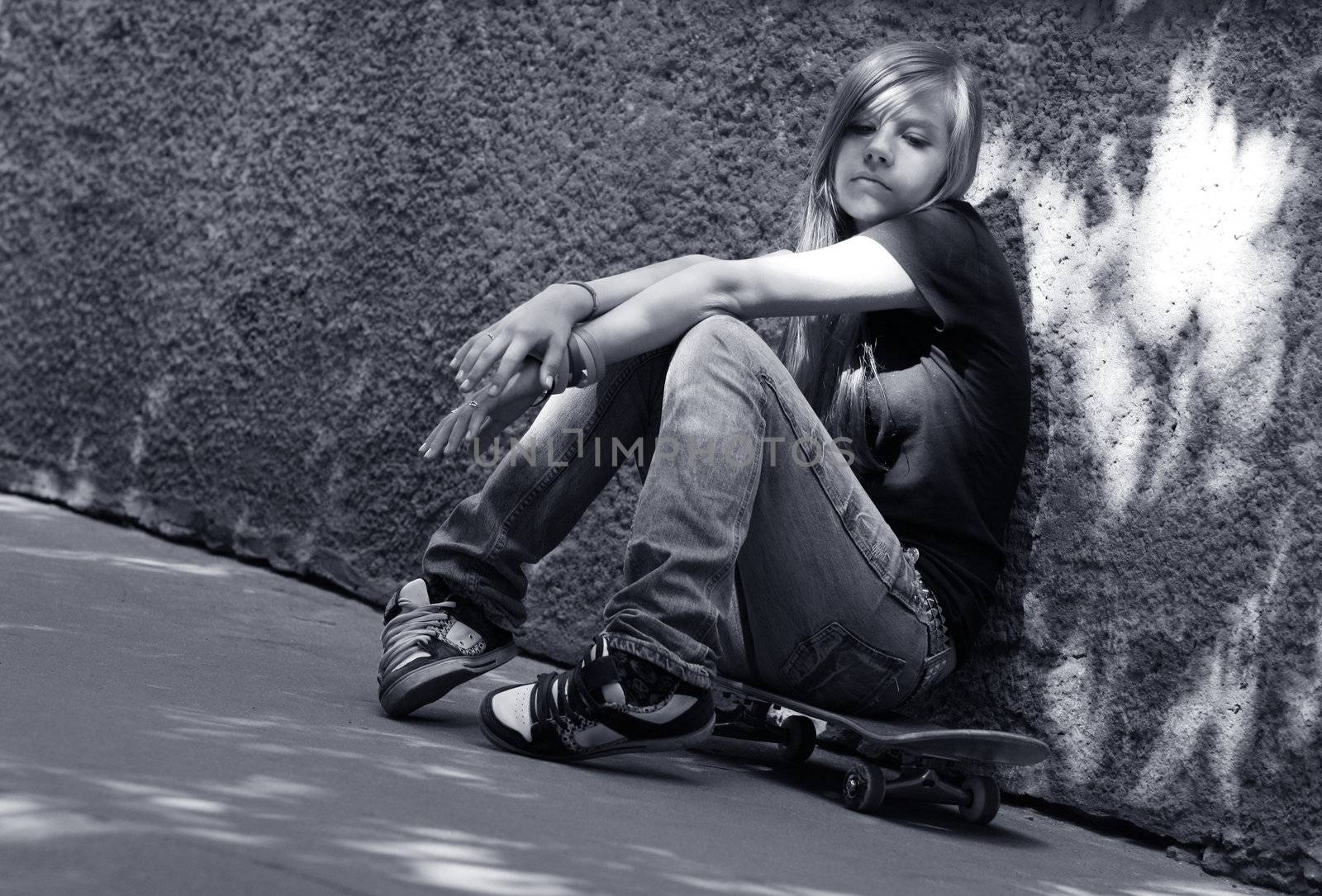 The girl with skateboard sitting against a wall. Shadow on a wall as a wing