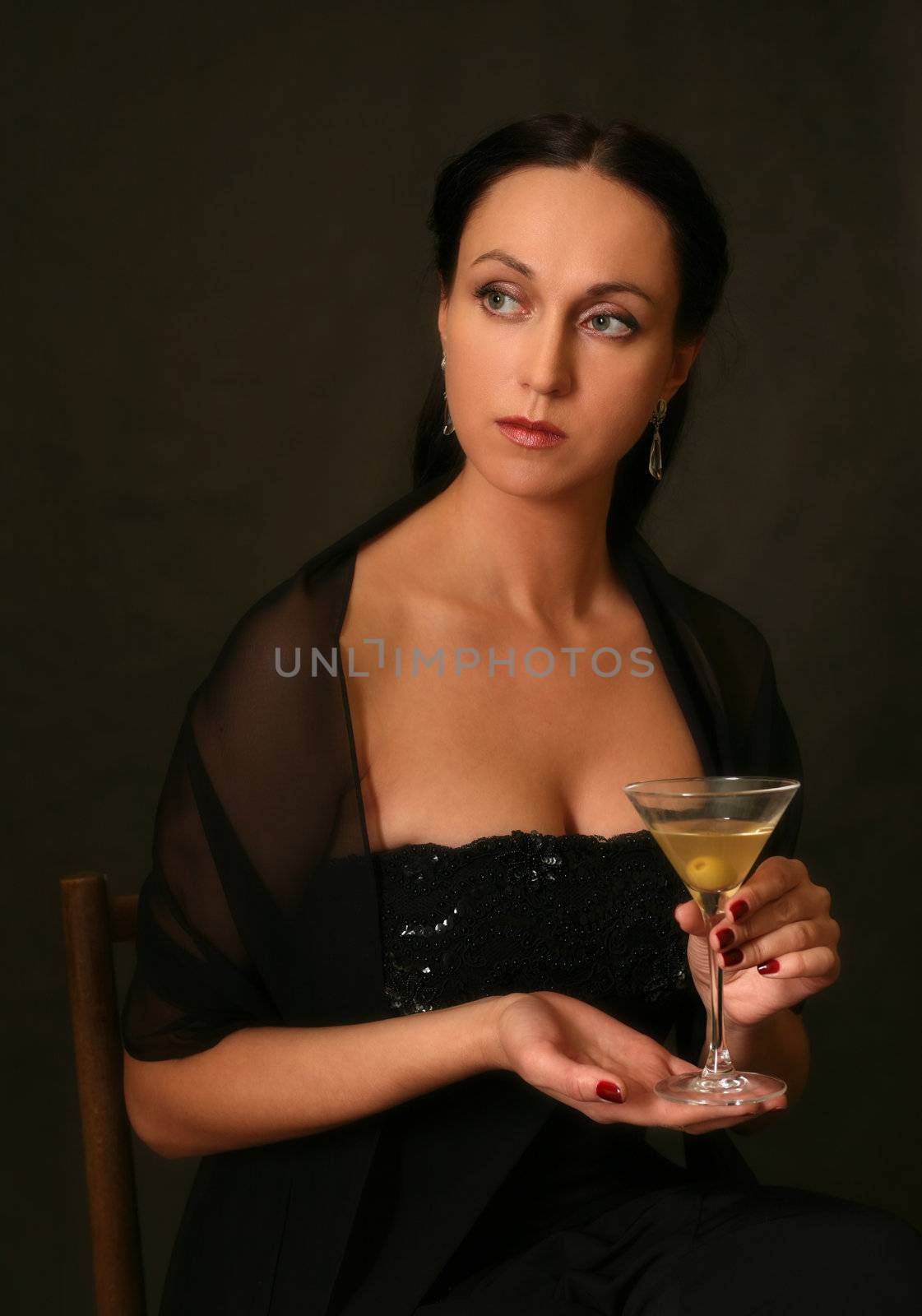 The beautiful woman with a glass of martini on a dark background