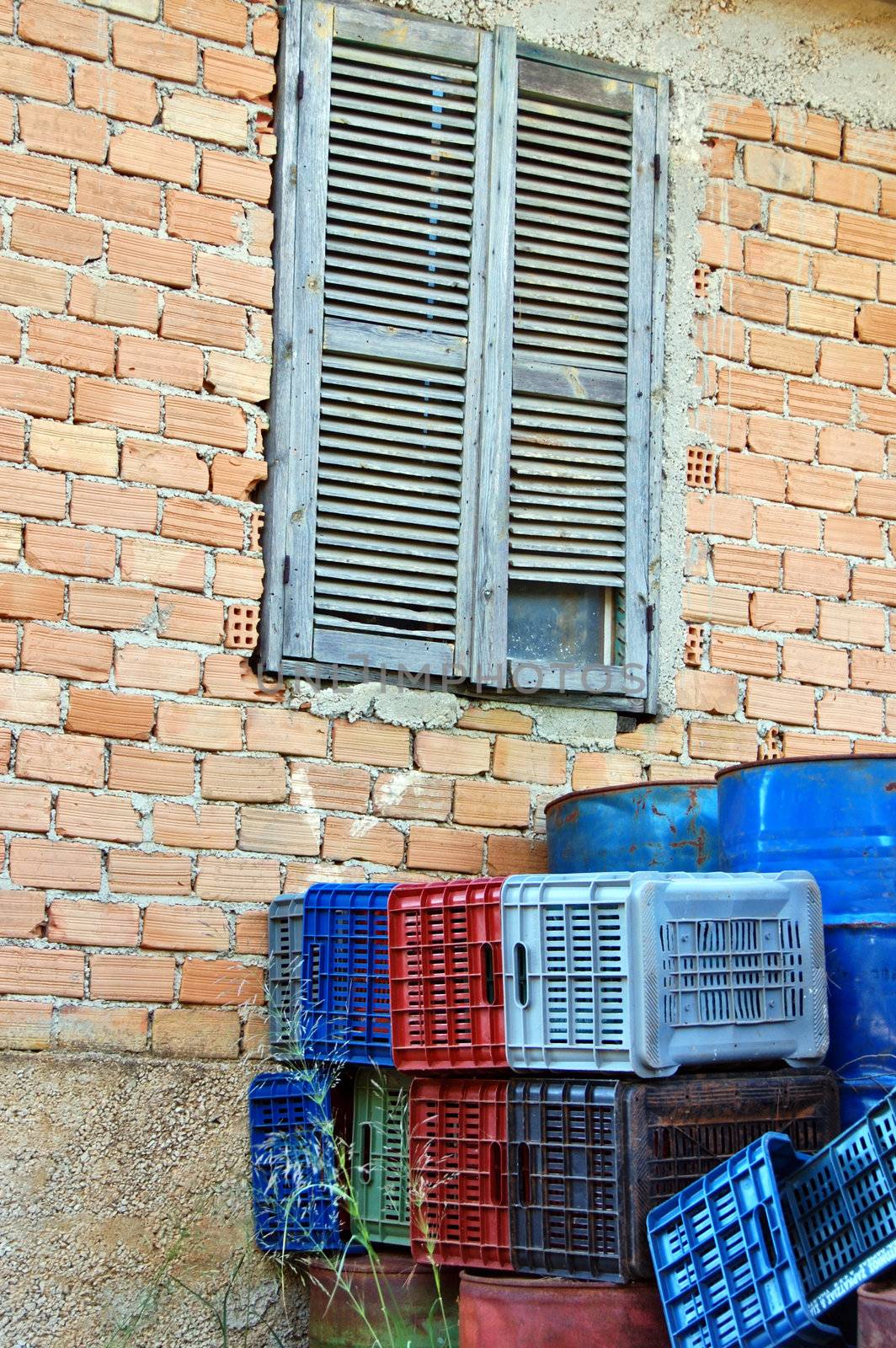 Abandoned house window and brick wall. Rusty metal barrels, plastic crate containers.