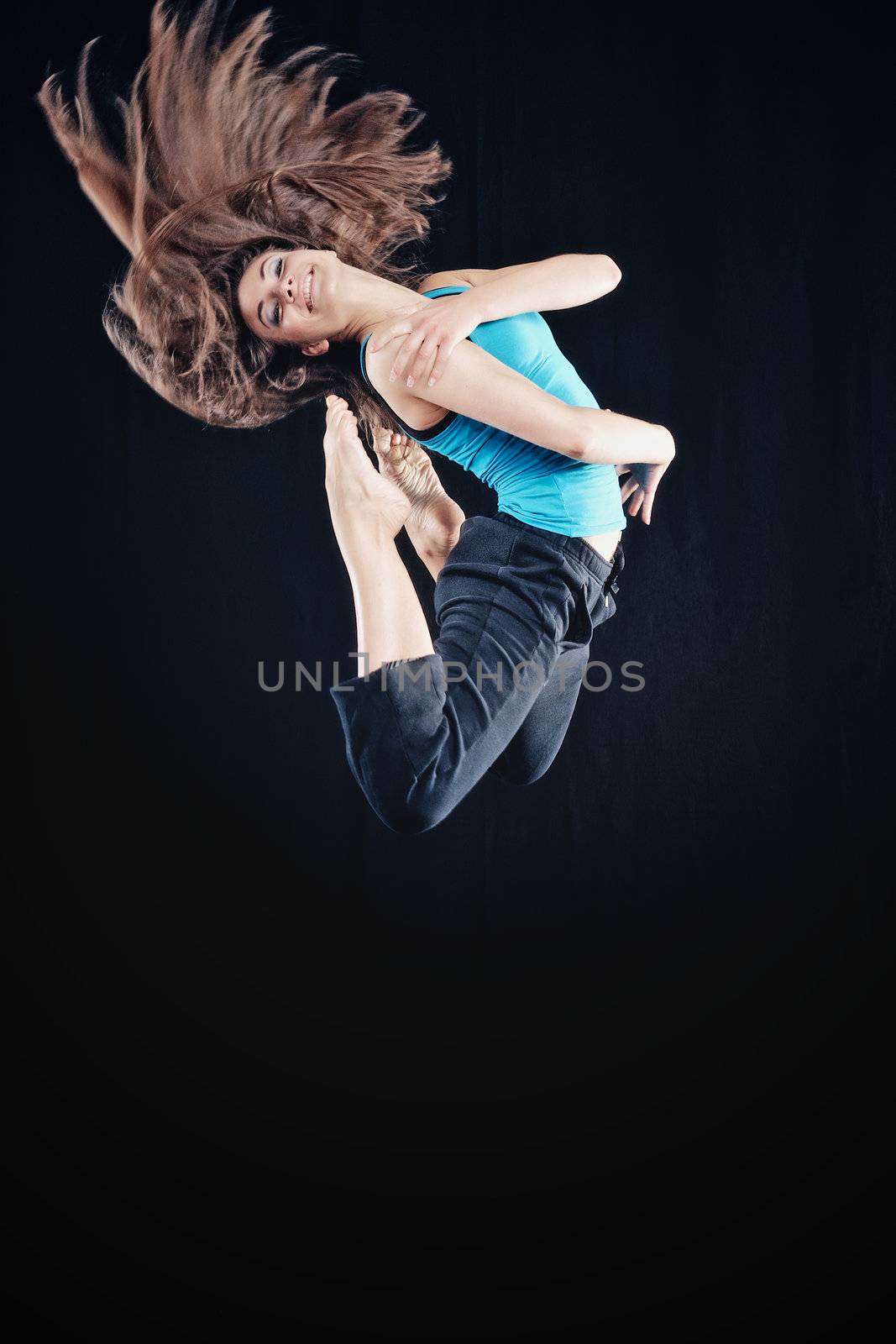 Young woman in tracksuit jumping on black background