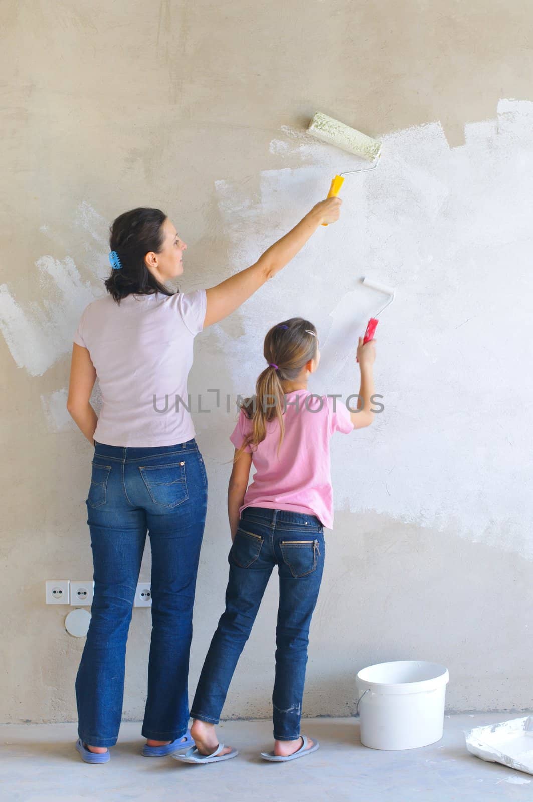 smiling Mother and douther painting a wall with roller