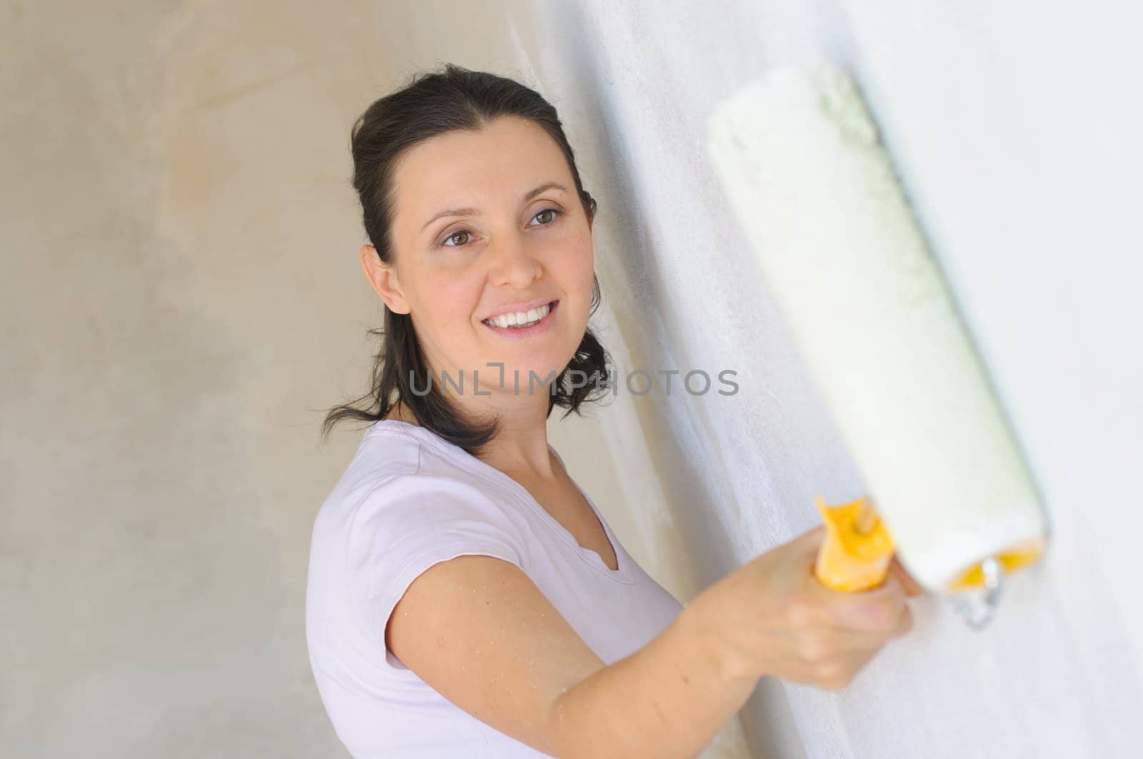 Young Woman painting a wall with roller .