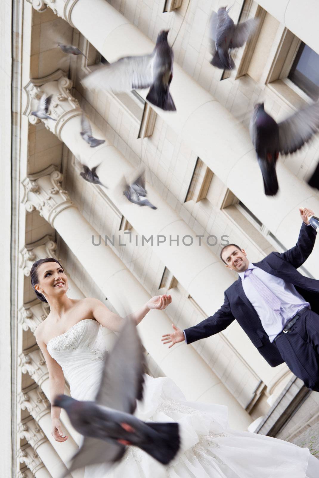 Happy bride and groom smiling behind flying pigeons