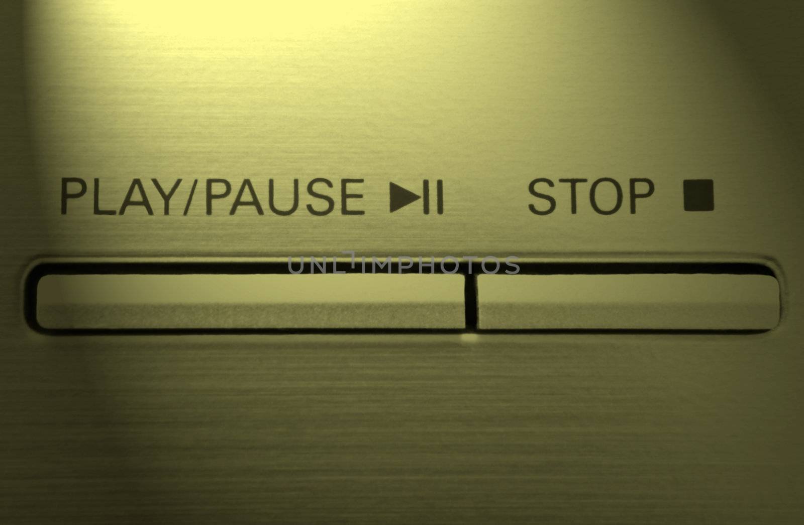 Close up on two buttons on a chrome electronic device with the words 'play/pause' and 'stop' with yellow light effect filter