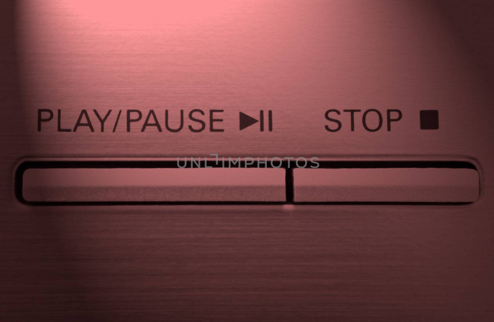 Close up on two buttons on a chrome electronic device with the words 'play/pause' and 'stop' with red light effect filter