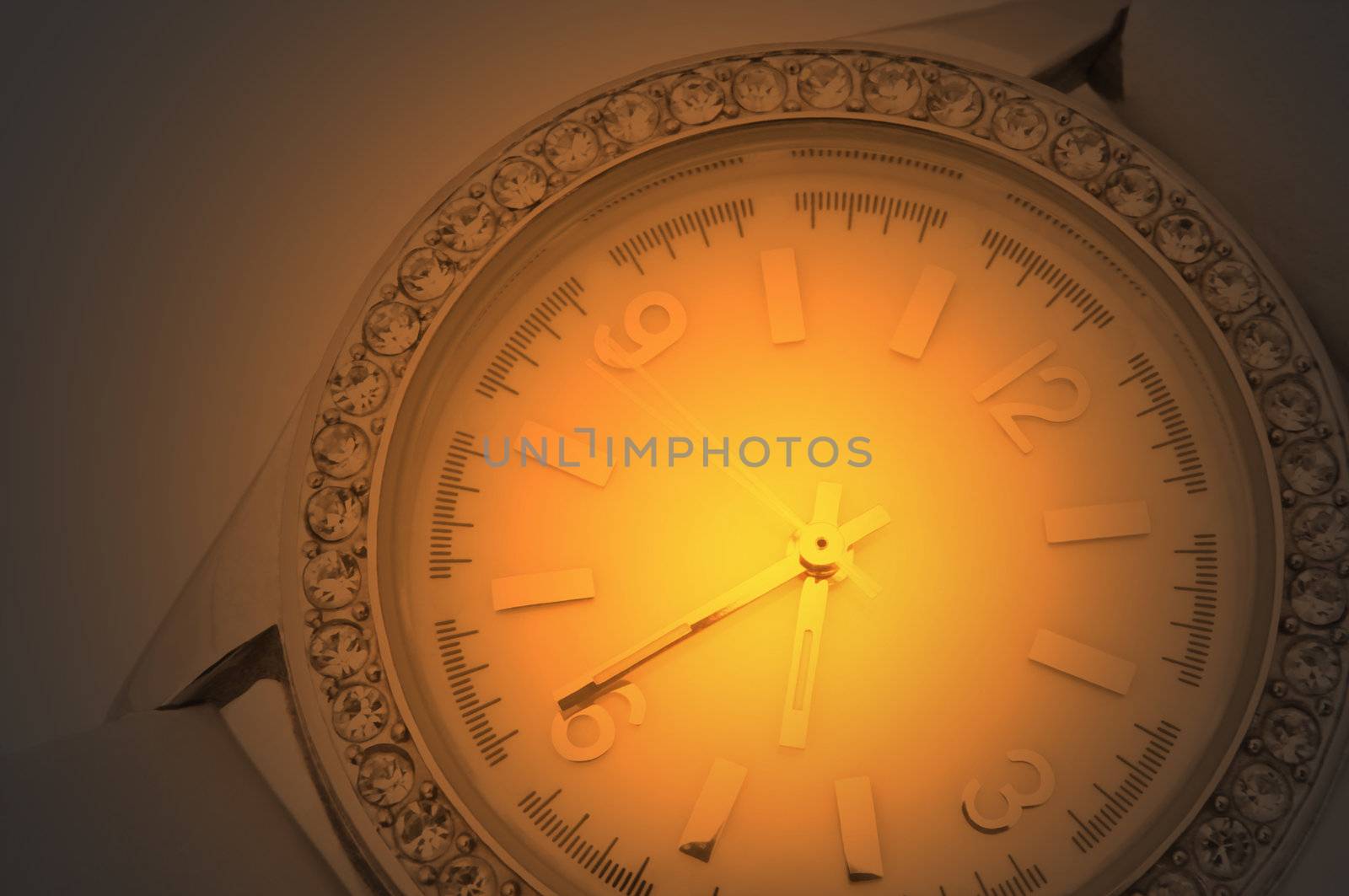 Close up capturing a white and chrome watch face with diamond surround over golden light effect filter.