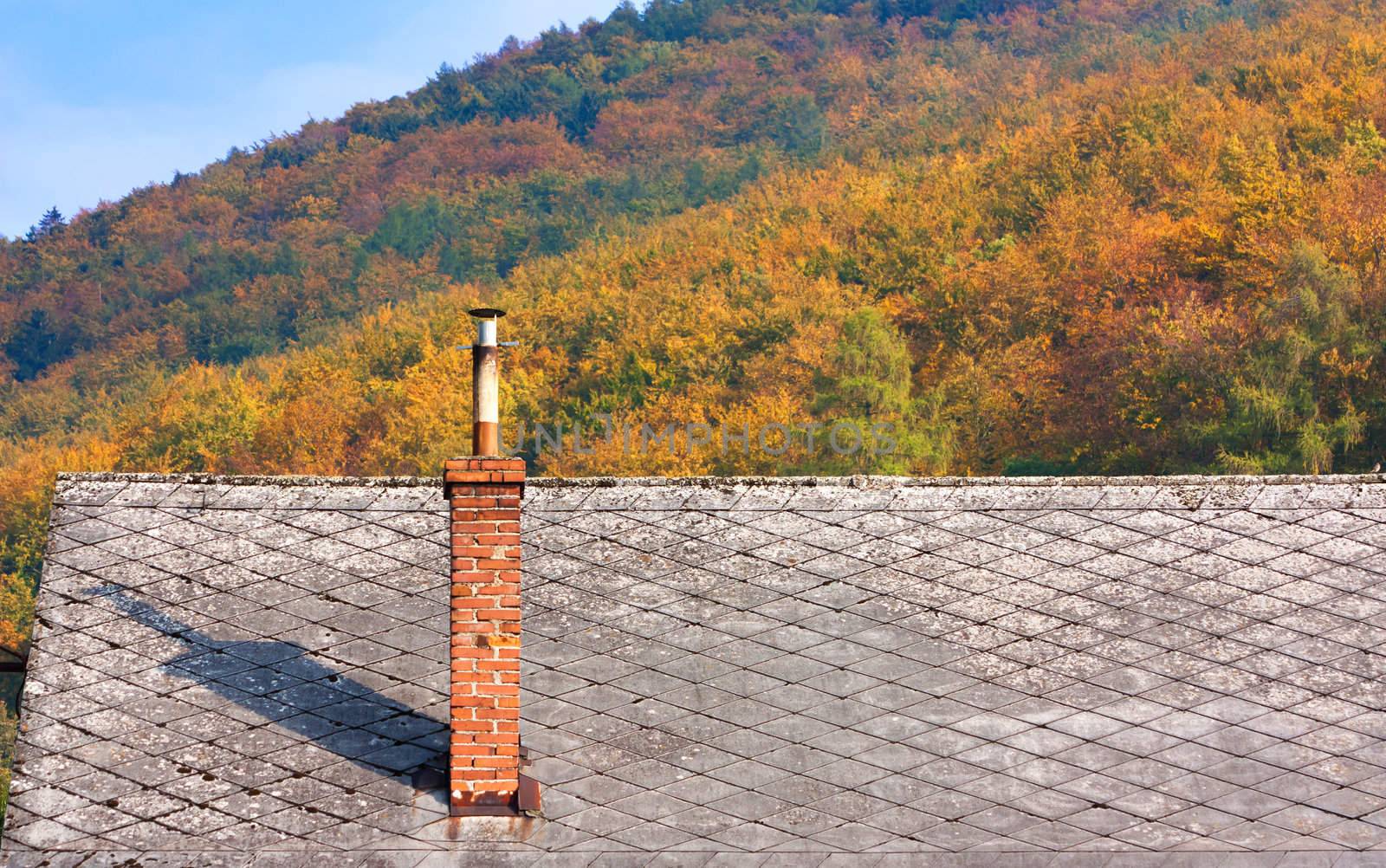 Peaceful landscape of autumn in low mountains with the roof and chimney of a house