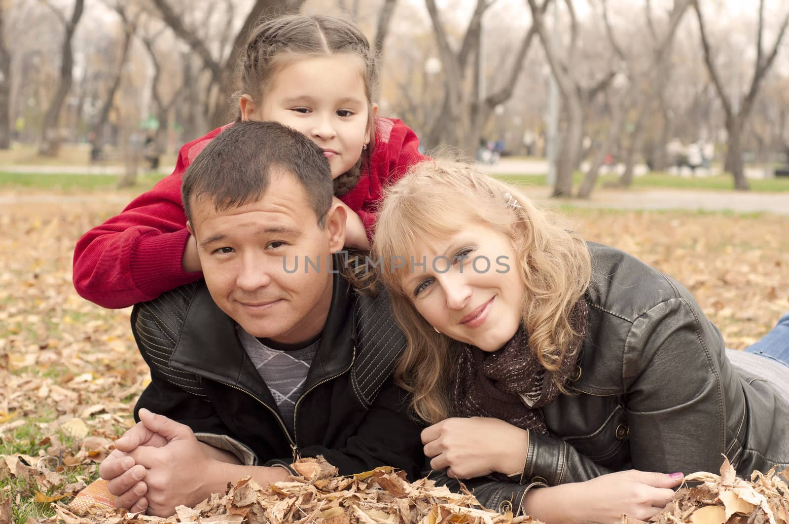 The young family in park, sits on a grass and smiles