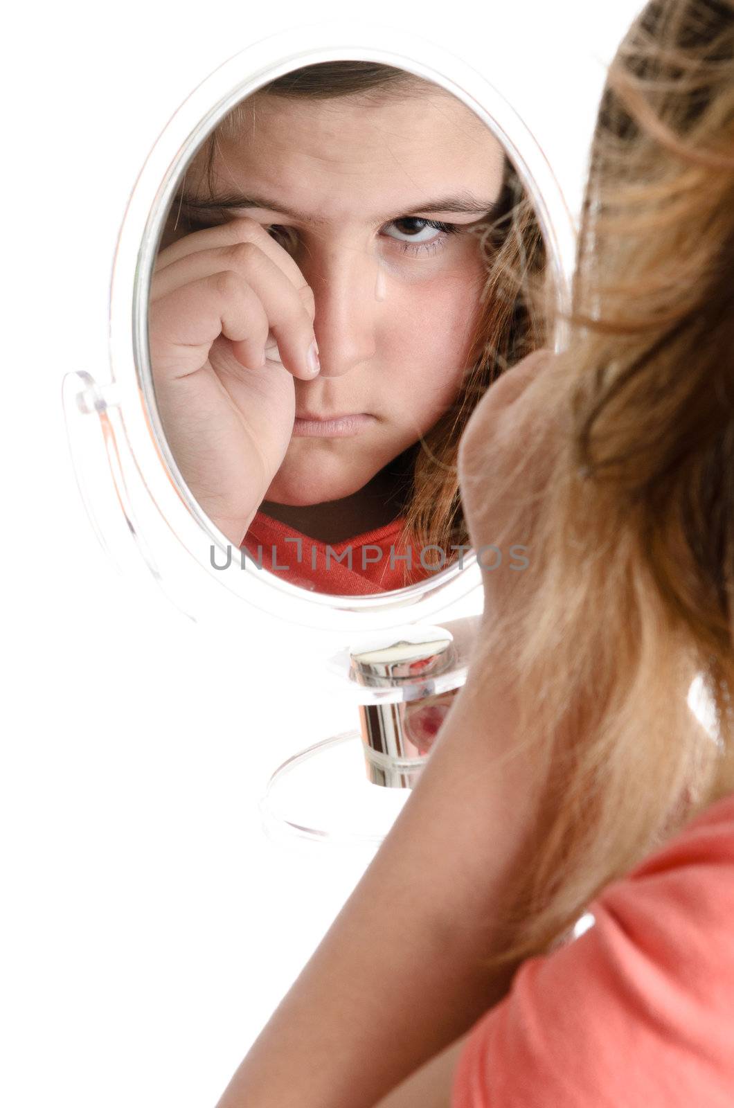 A sad girl is crying while looking at the viewer in a mirror, isolated against a white background.