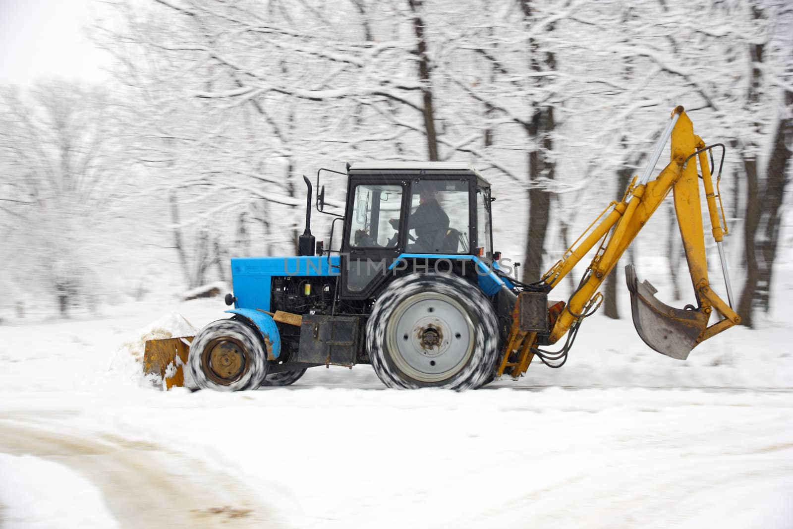 The tractor of dark blue color deletes snow in park