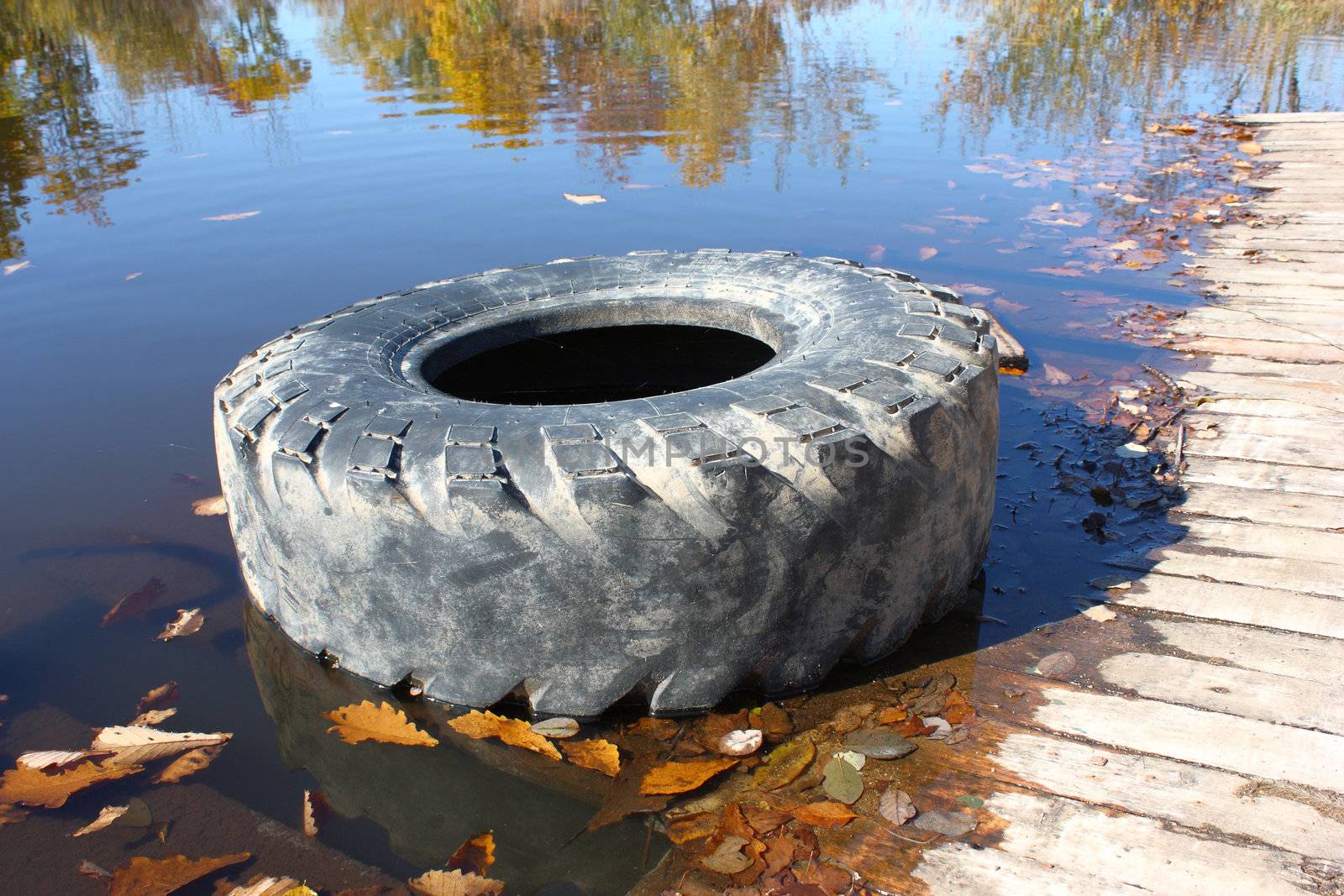 The big old tire from the lorry lies on the bank of beautiful lake in the autumn.